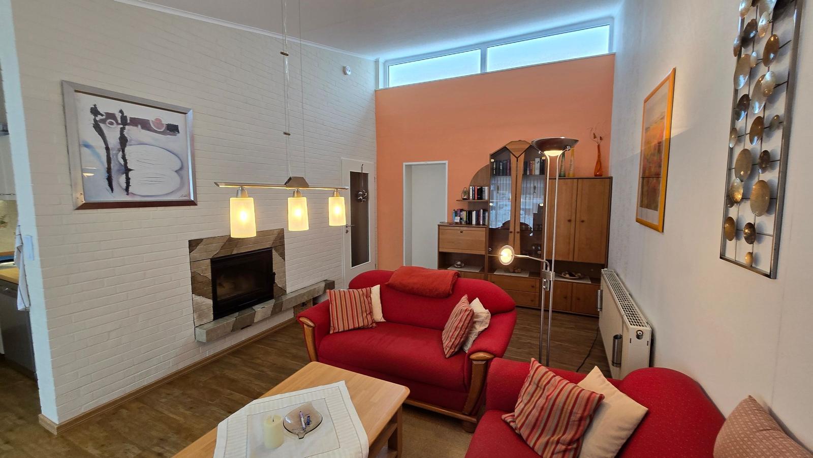 Wohnzimmer mit rotem Sofa, Kamin und Holzboden.