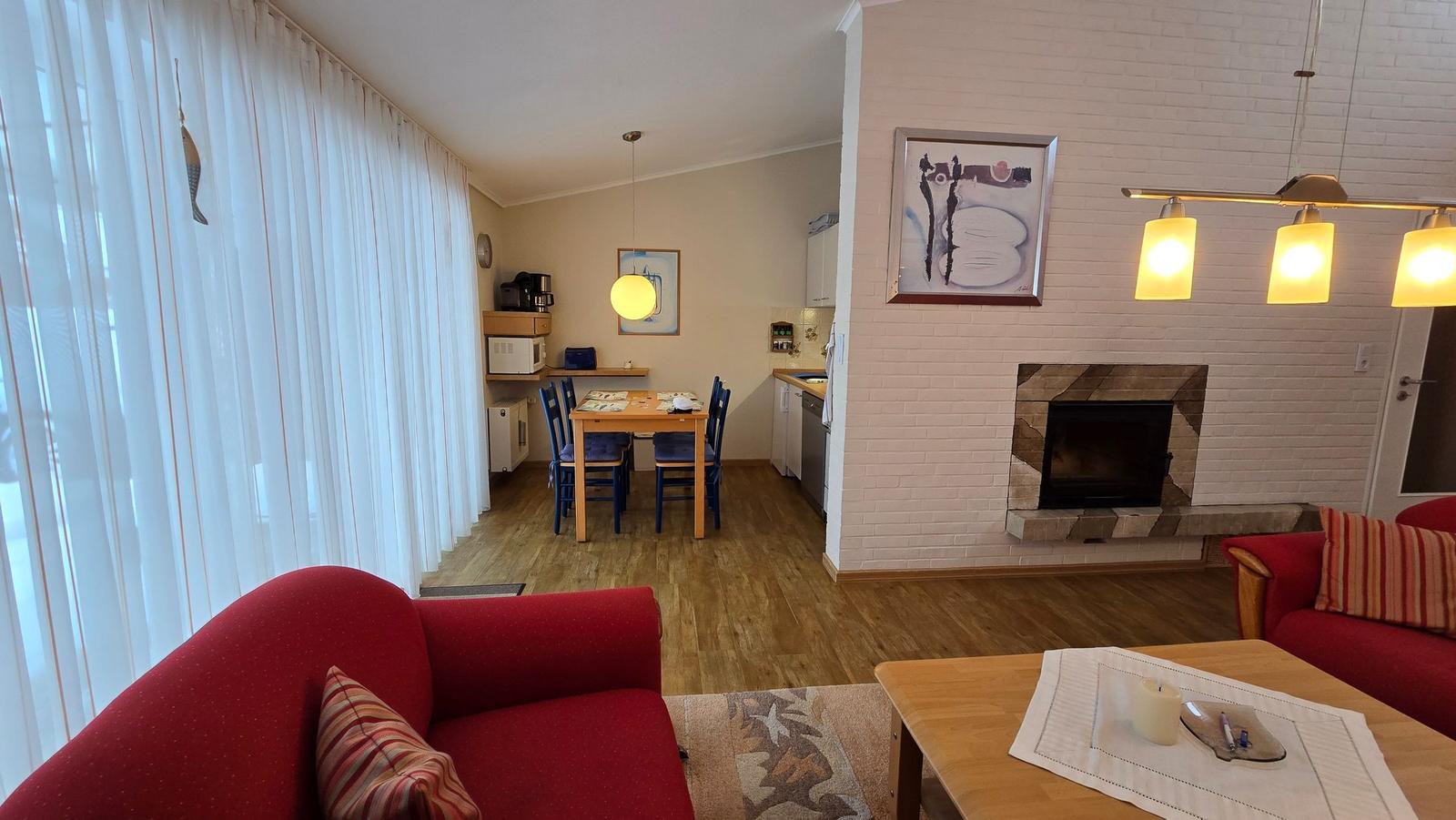 Wohnzimmer mit Kamin, Essbereich und Küche. Rote Sofas und Holzboden.