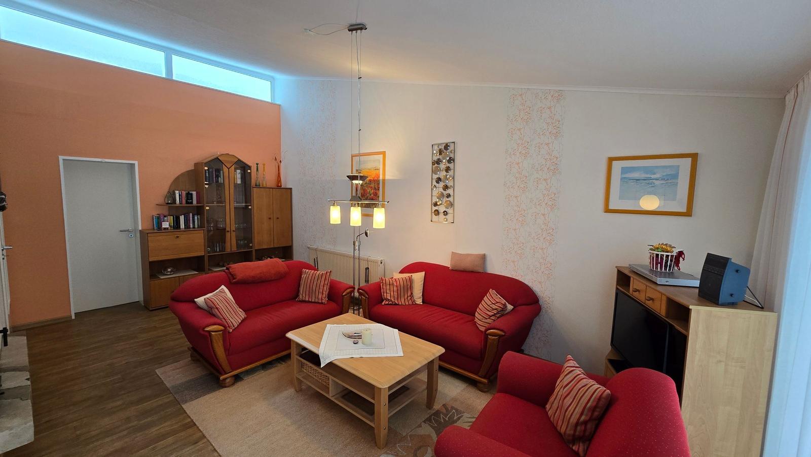 Wohnzimmer mit zwei roten Sofas, Tisch und Fernseher.
