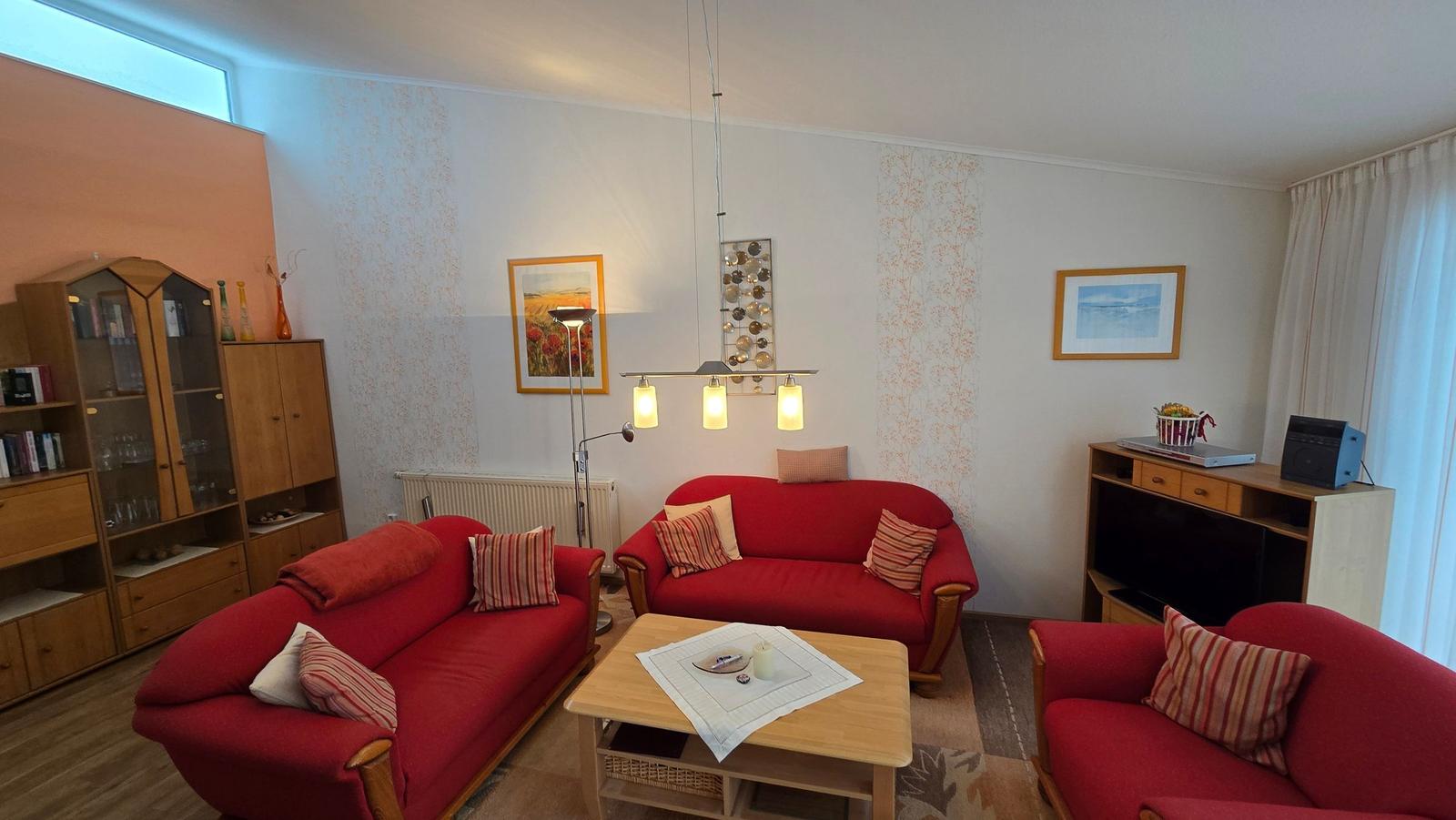 Wohnzimmer mit zwei roten Sofas, Holztisch und Wandbildern.