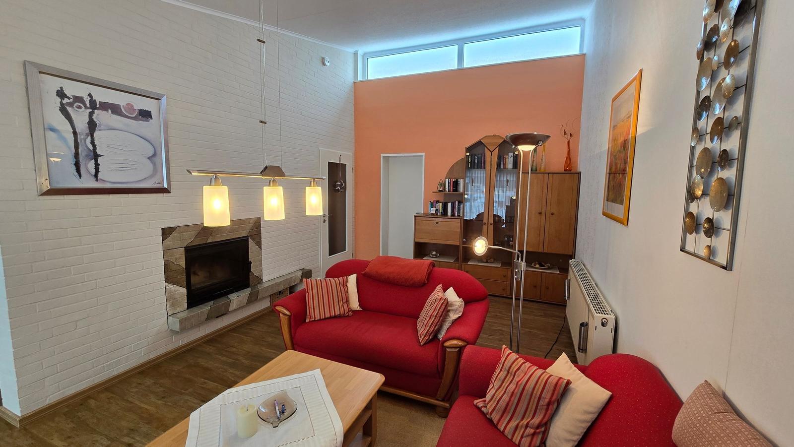 Wohnzimmer mit rotem Sofa, Kamin und Holzboden.