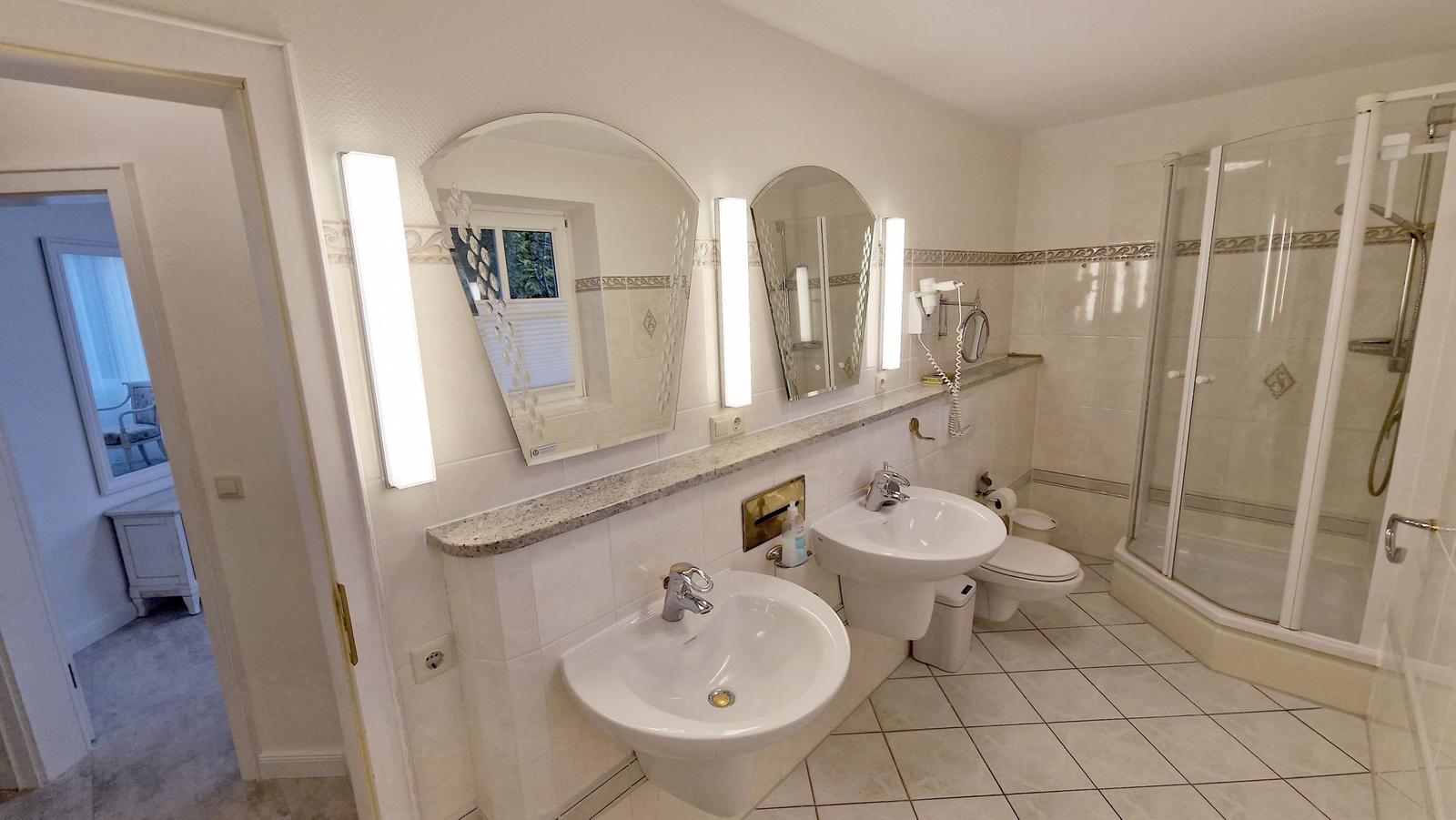 Badezimmer mit Dusche, zwei Waschbecken und Spiegeln