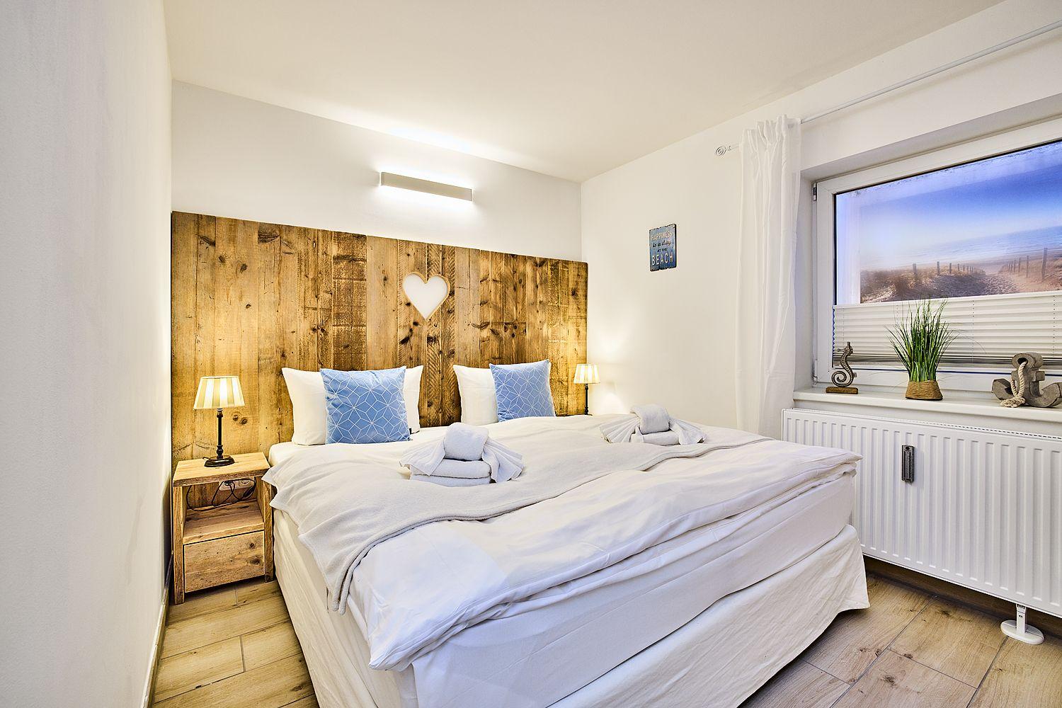 Schlafzimmer mit Holzbett, Fenster und Strandbild.