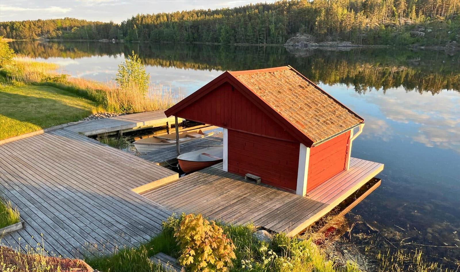 Rotes Bootshaus am See mit Holzsteg und zwei Booten.