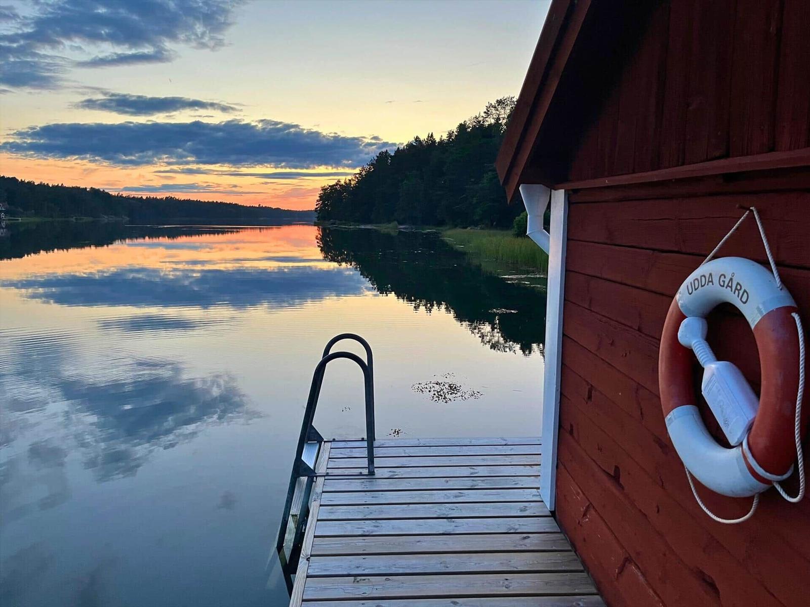 Roter Holzhaus mit Rettungsring an der Wand und Bootssteg zum See.