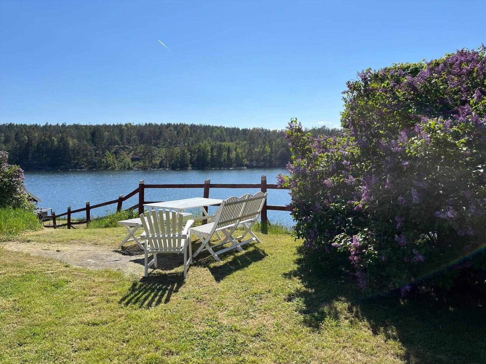 Terrasse mit Tisch und Stühlen am See mit Lilienhecke.