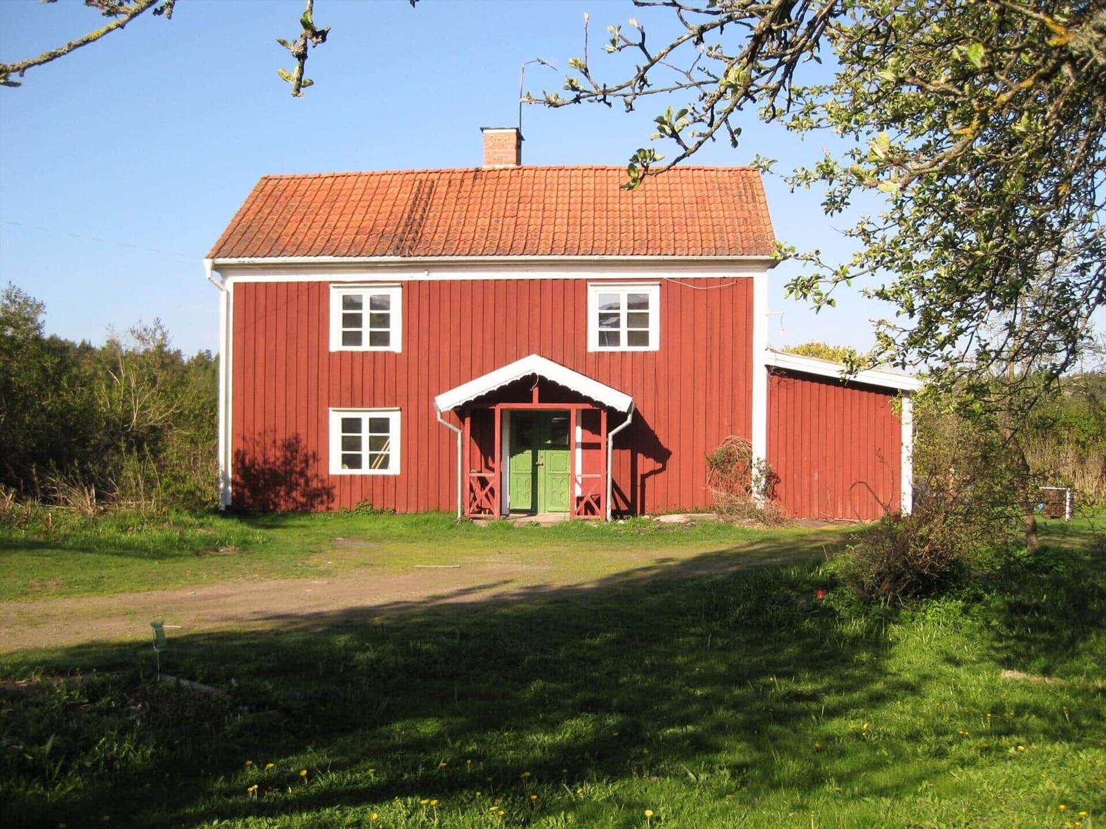 Rotes Holzhaus mit grüner Tür und rotem Dach unter Bäumen.