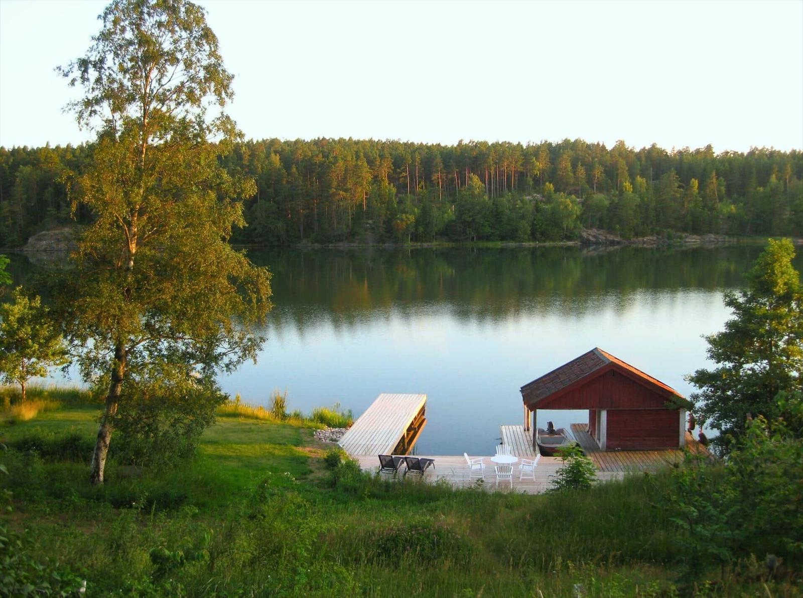 Rotes Bootshaus am See mit Holzterrasse und Liegestühlen.