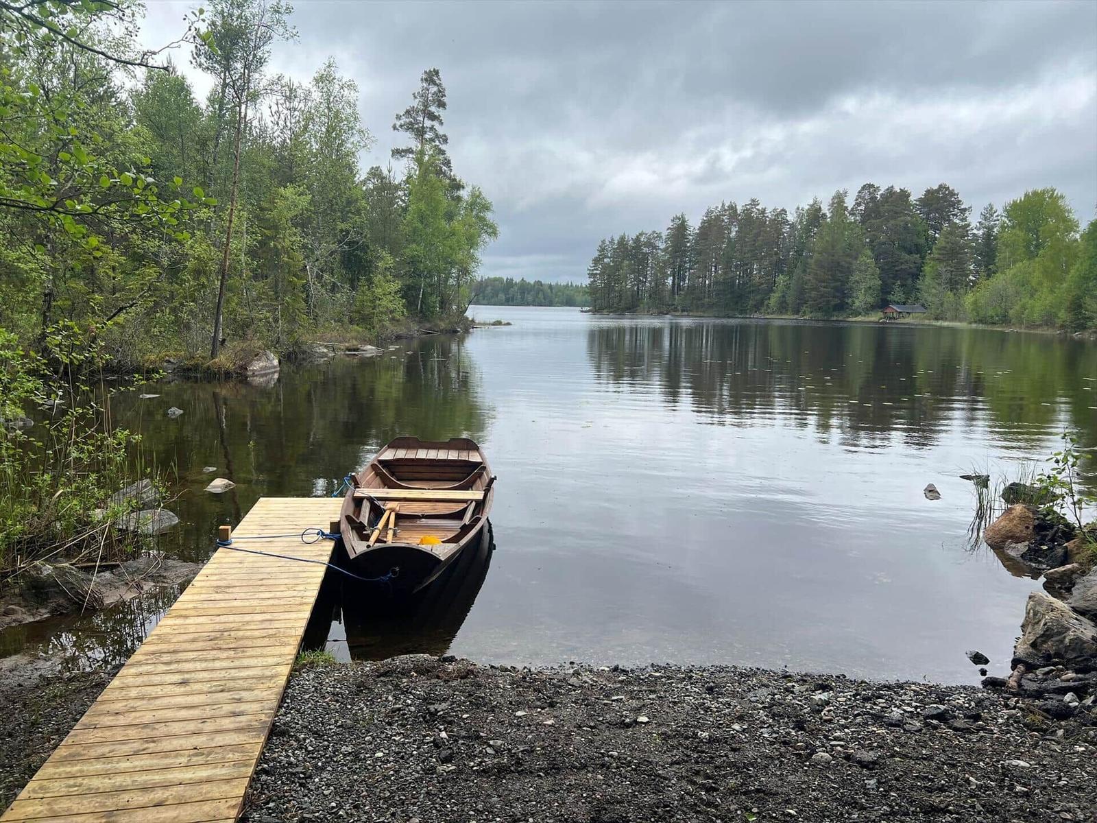 Holzboot liegt am Steg eines Sees mit Uferbereich aus Kies.