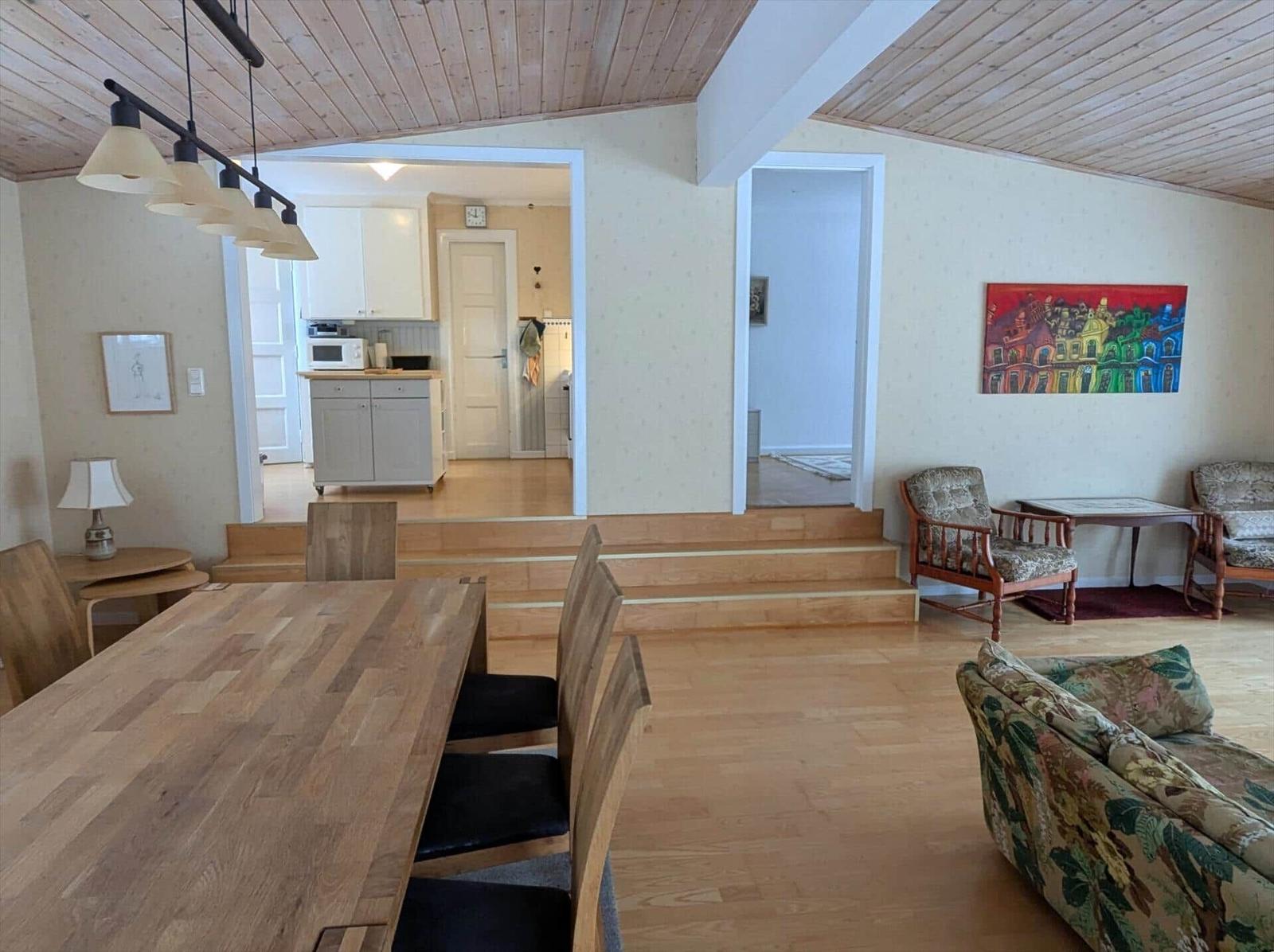 Essbereich mit Holztisch, Wohnzimmer mit Sofa und Stühlen, Küche im Hintergrund.