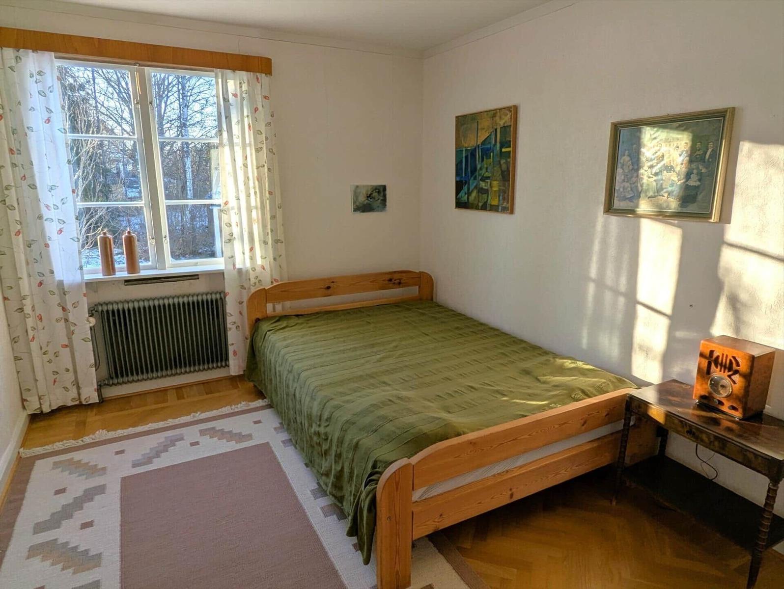 Schlafzimmer mit Holzbett, Fenster und Wandbildern.