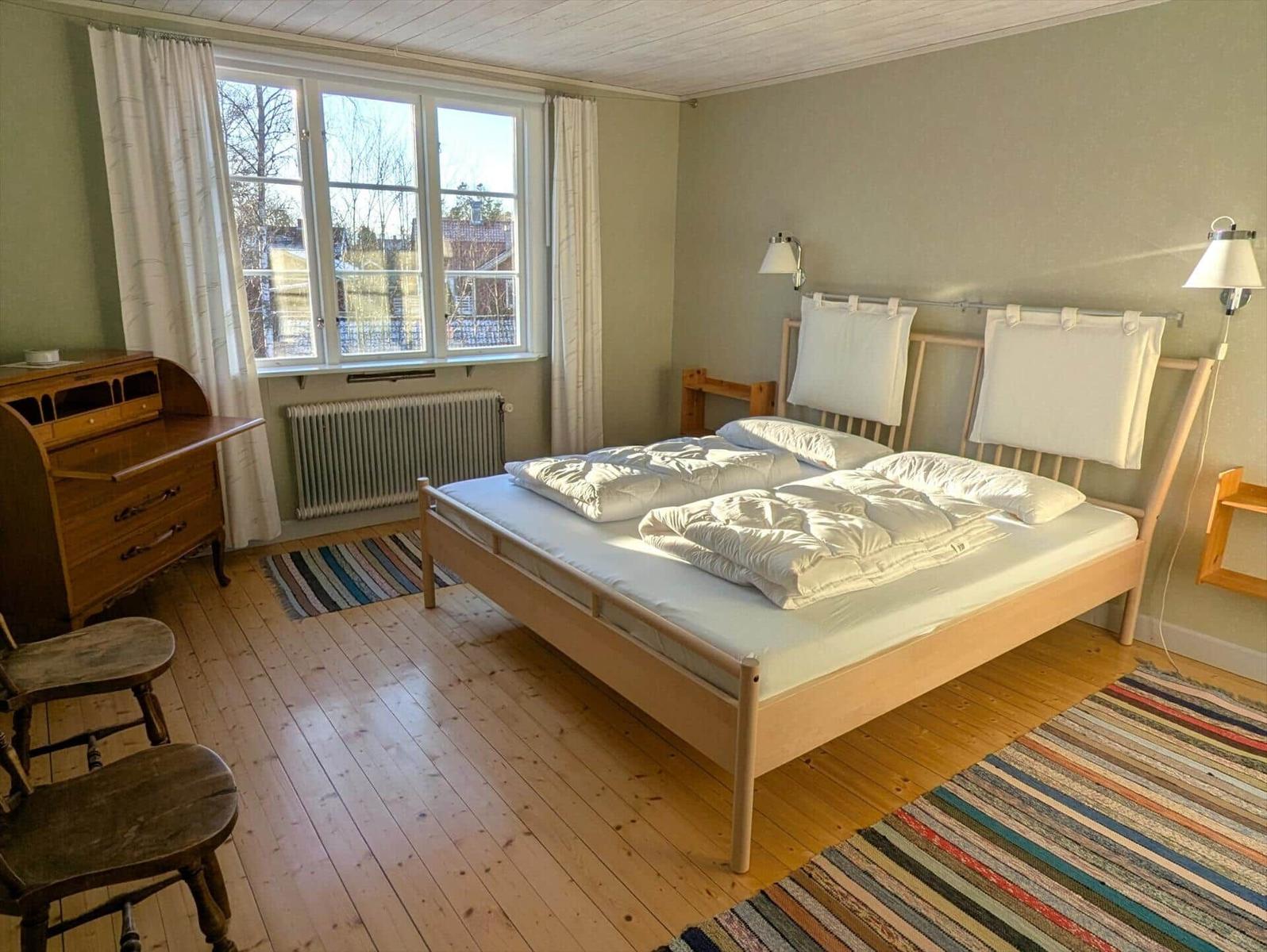 Schlafzimmer mit Holzboden, Bett und Fenster. Holzmöbel und Wandlampen.