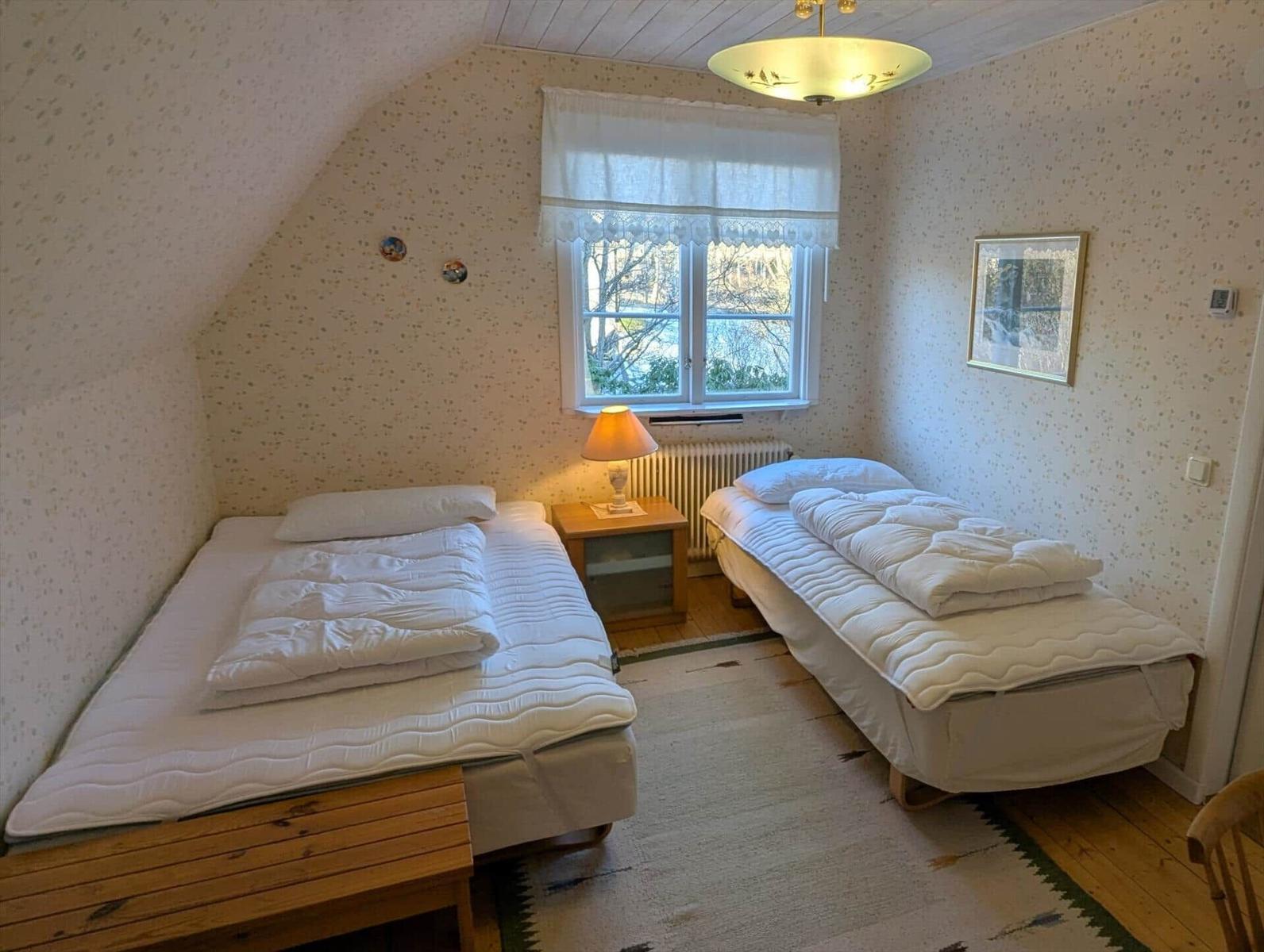 Zwei Betten, Fenster, Nachttisch, Decken und Wandtapete.