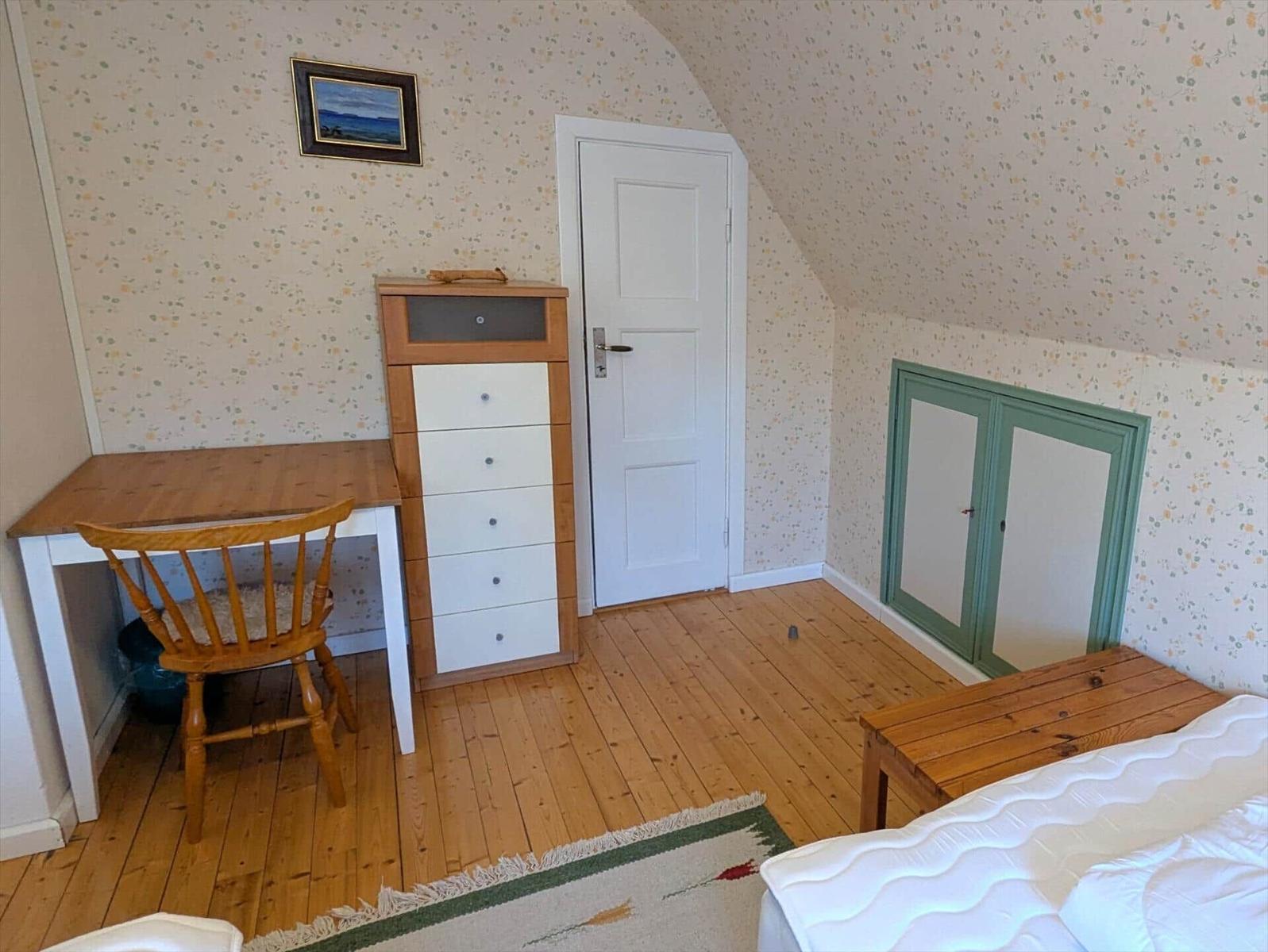 Schlafzimmer mit Holzboden, Schreibtisch, Bett und Kleiderschrank.