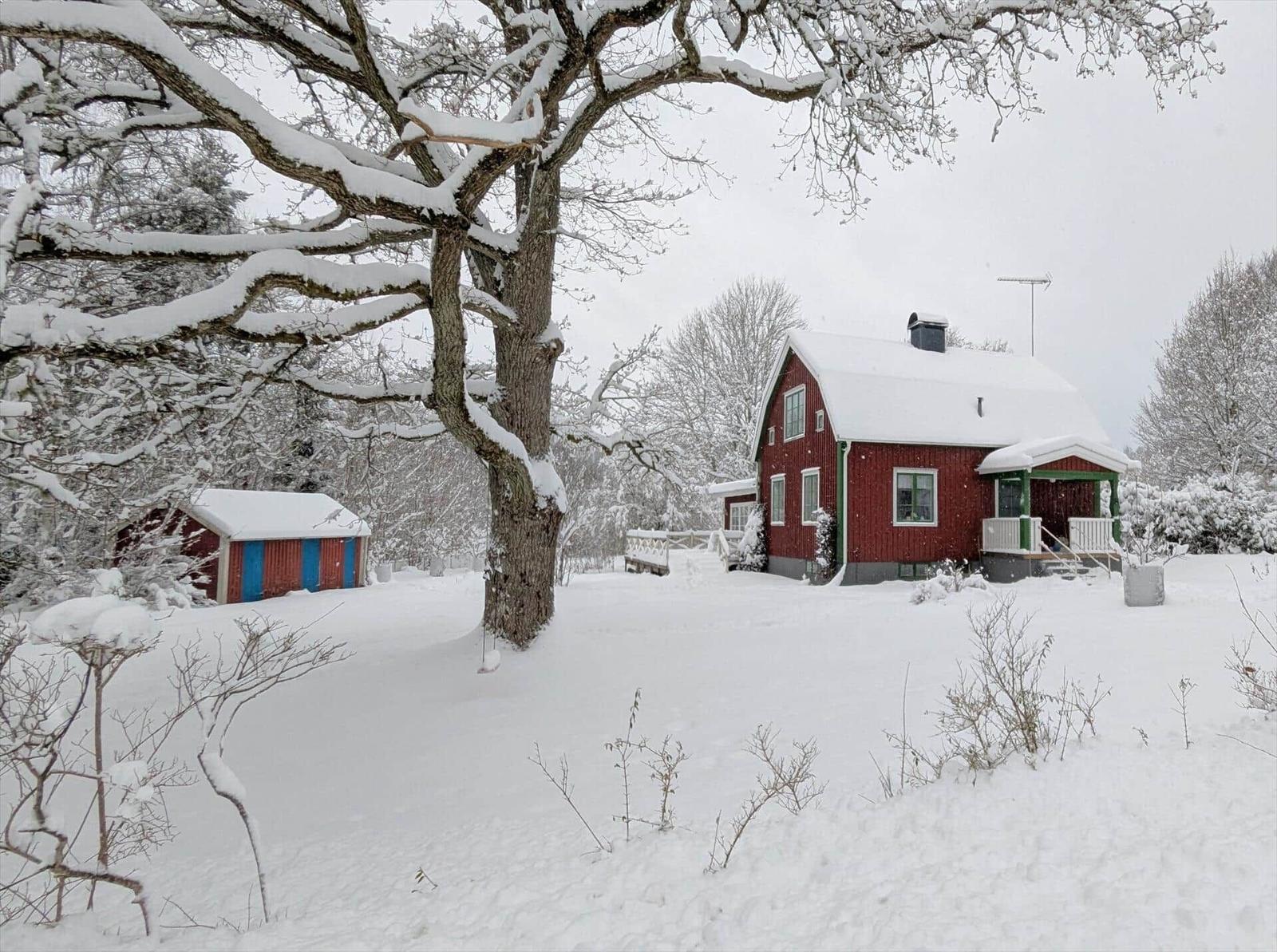 Rotes Haus mit Schneebedecktem Garten und kleinem Nebengebäude.