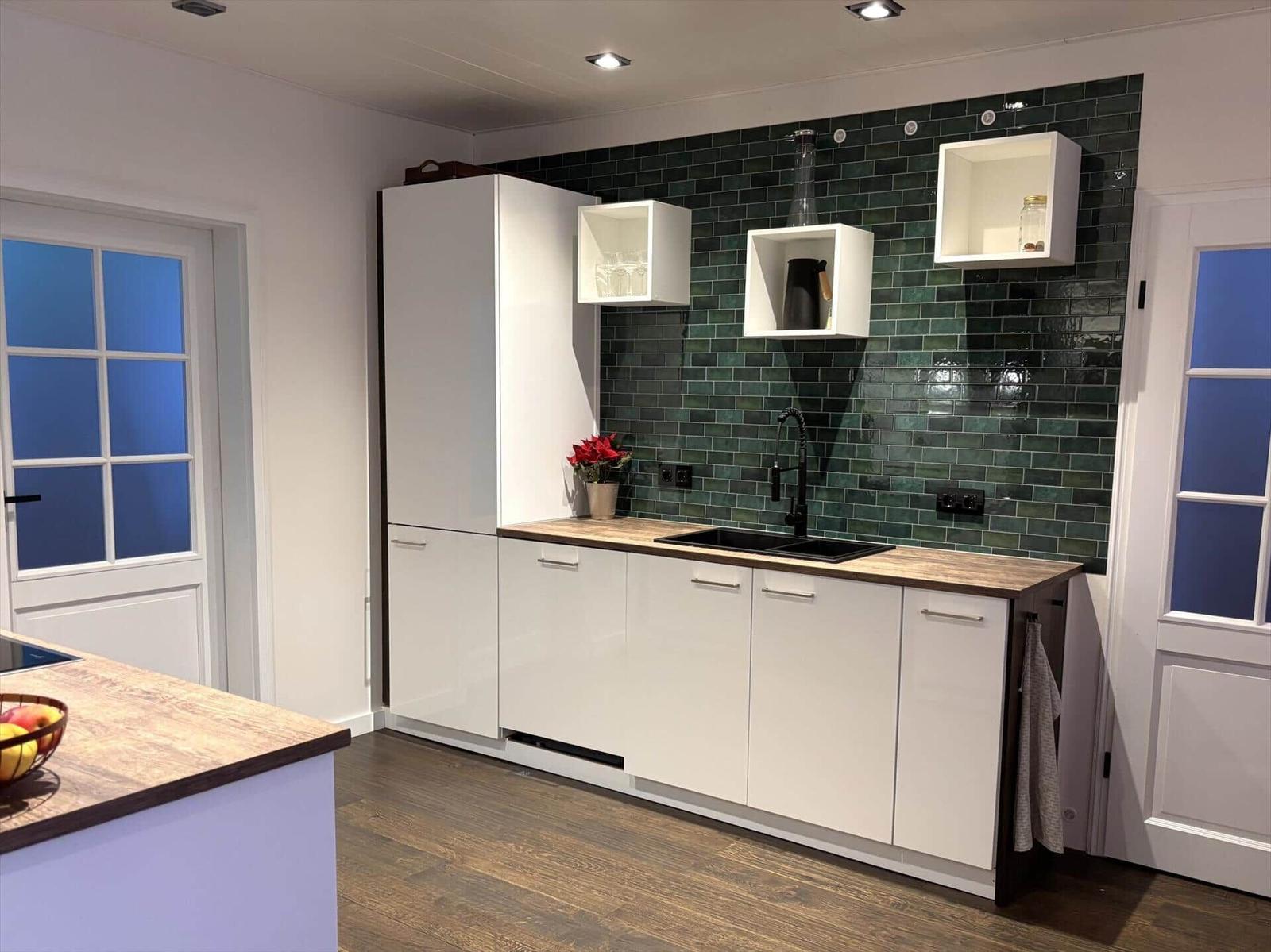 Küche mit weißen Schränken, grüner Fliesenspiegelwand und Holz Arbeitsplatte.