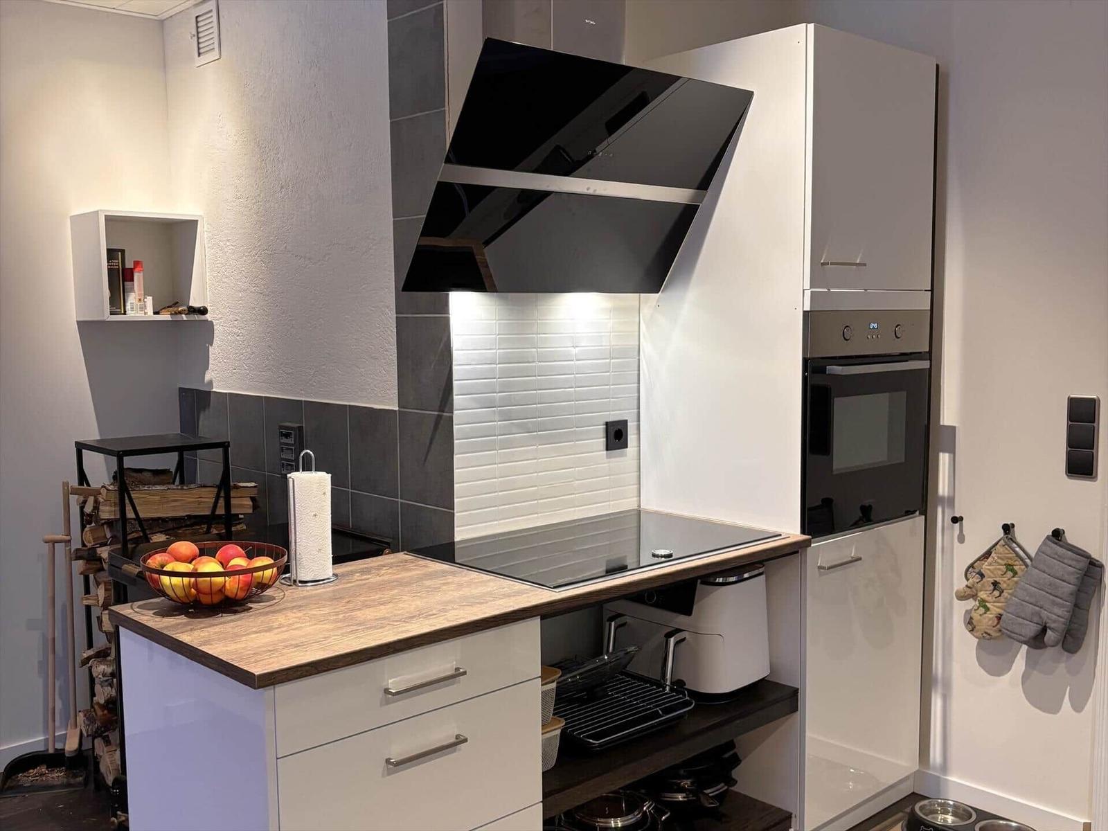 Moderne Küche mit Kochfeld, Backofen und Holz-Arbeitsplatte.