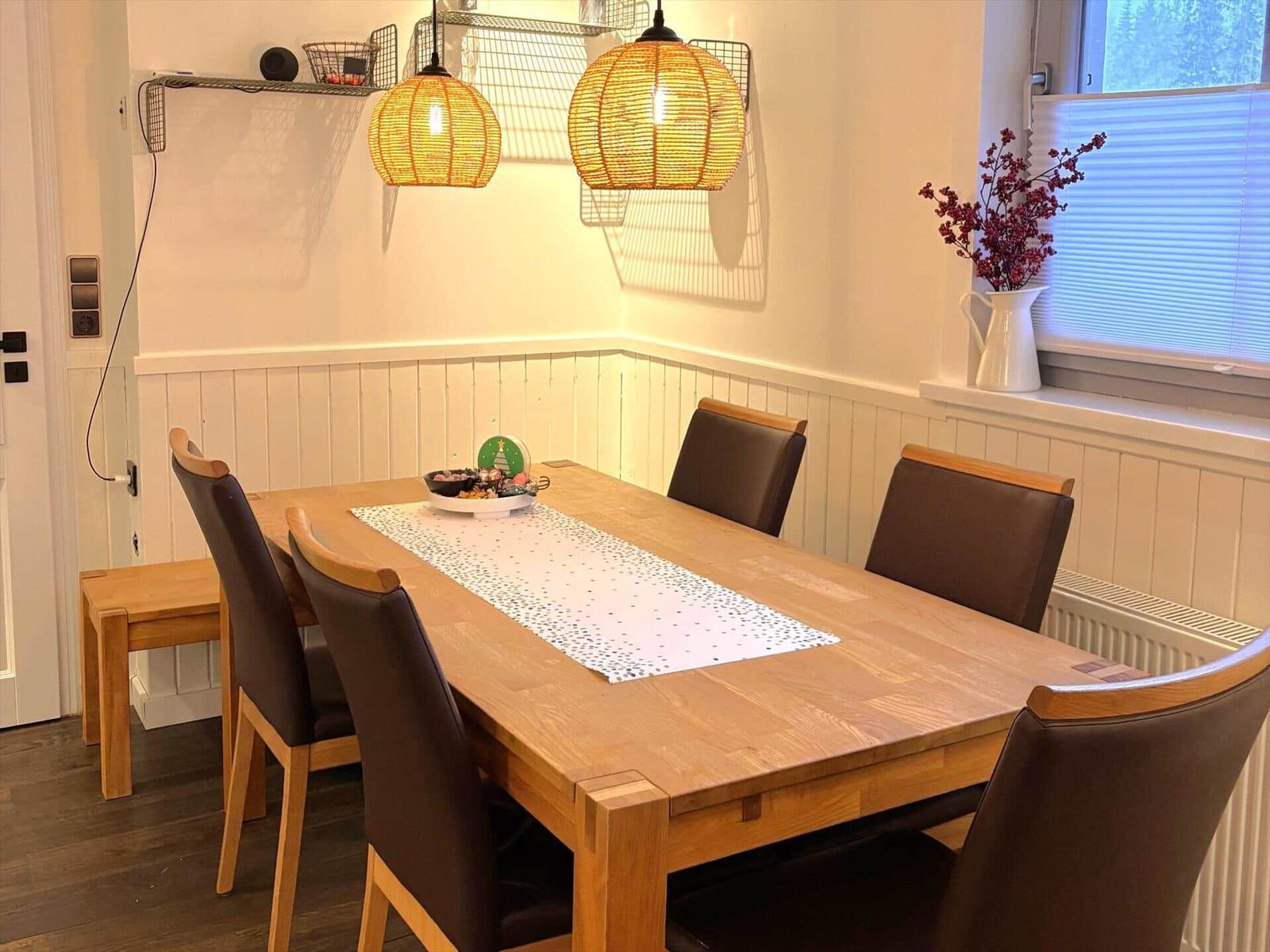 Esstisch mit sechs Stühlen, zwei Hängelampen und Fenster mit Blenden.