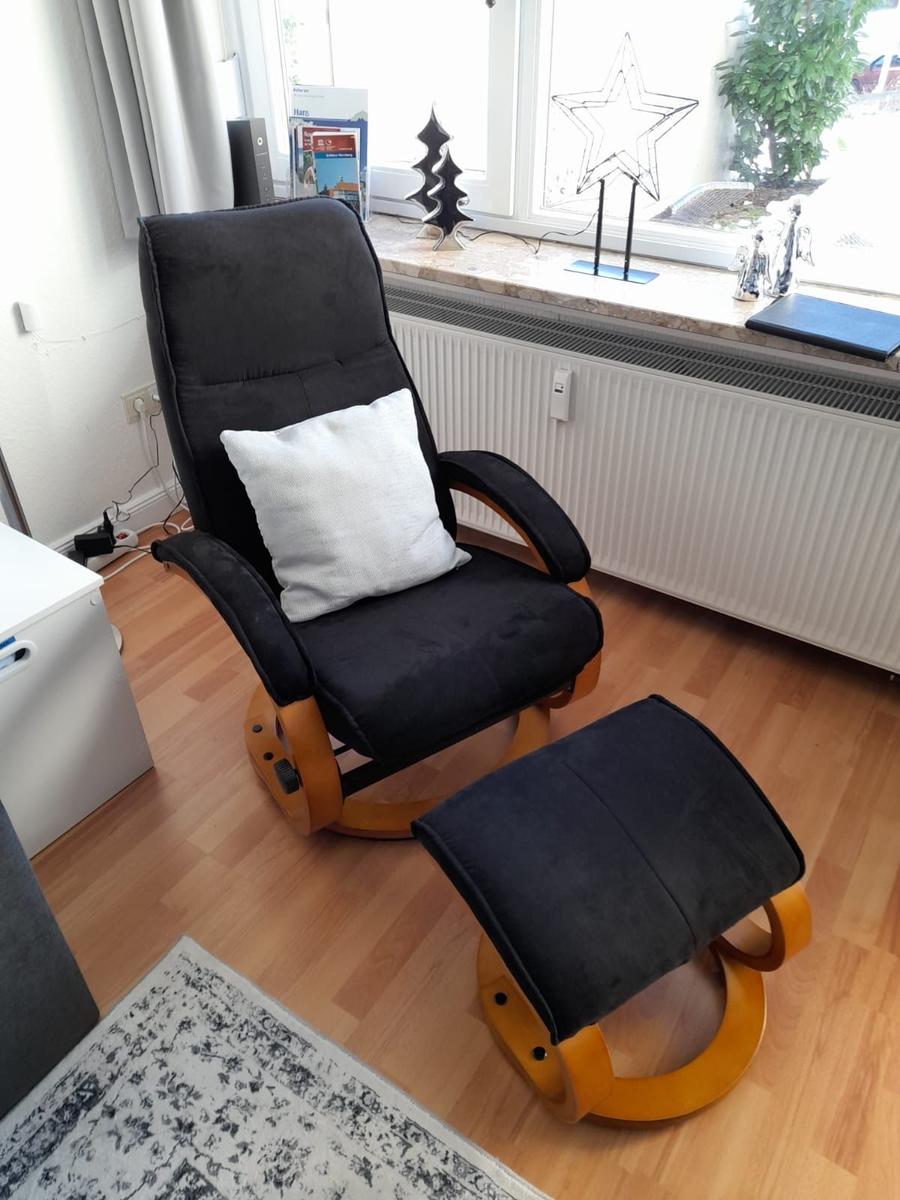 Schwarzer Sessel mit Kissen und Fußstütze vor Fenster mit Dekoration.