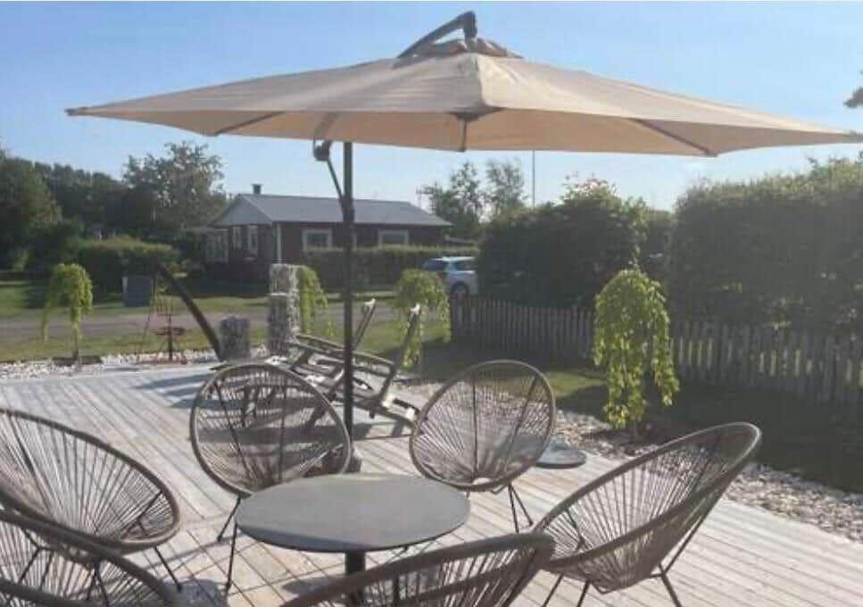 Terrasse mit Sonnenschirm und Rattanmöbeln. Hintergrund: Garten und Nachbarhaus.