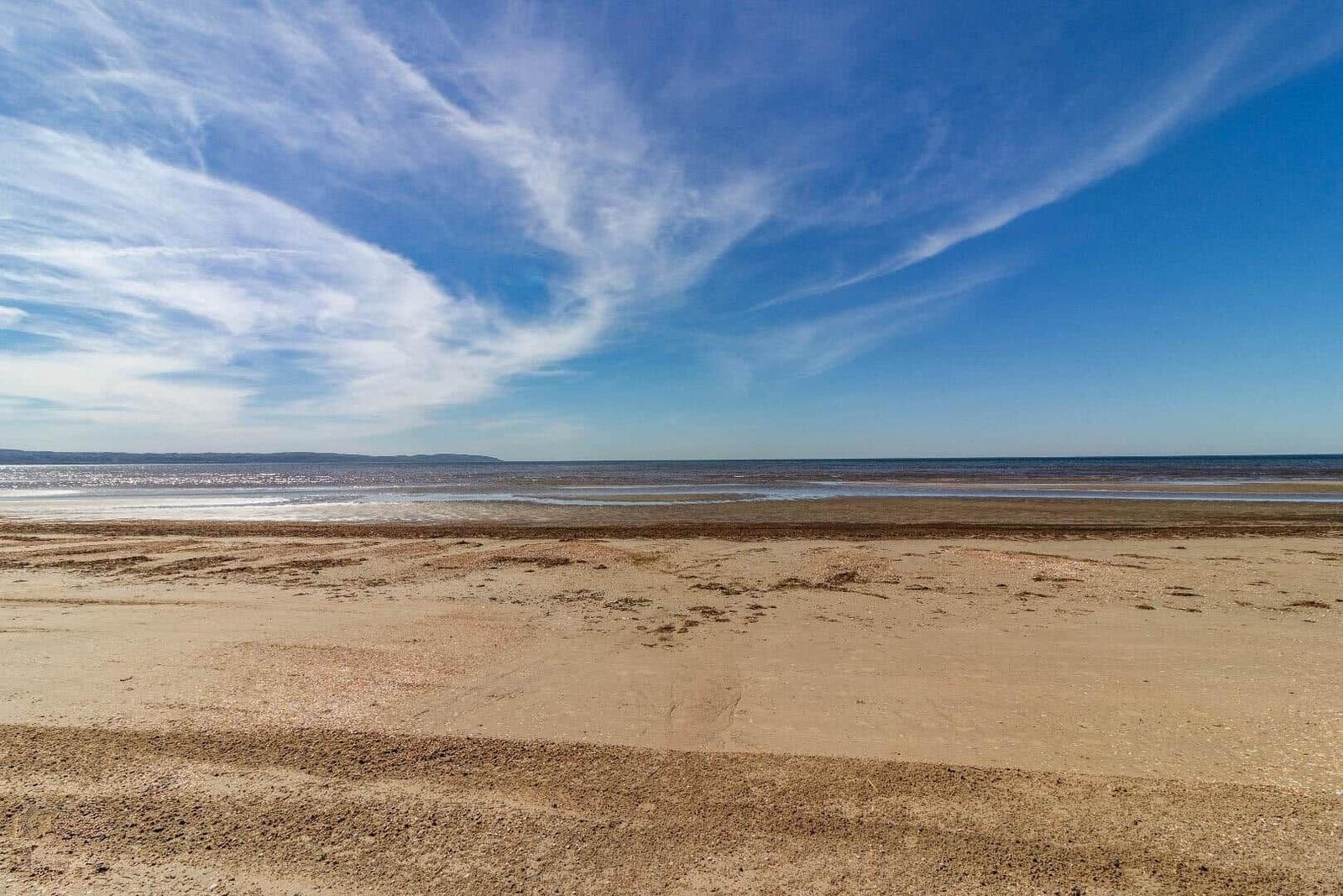 Strand mit Sand und Wasser unter blauem Himmel mit weißen Wolken.