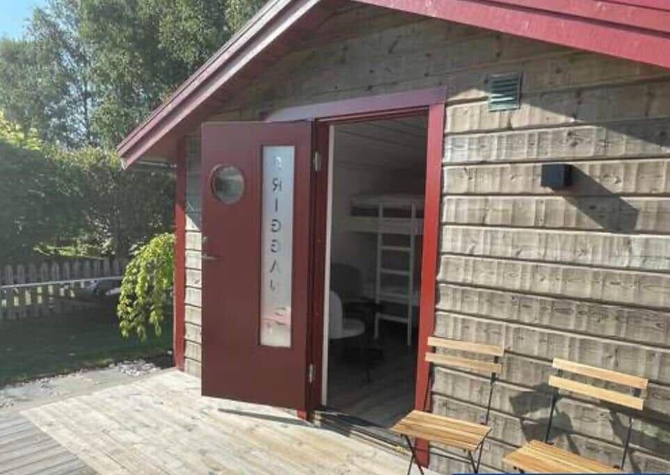 Holzgebäude mit offener Tür, darin sichtbarer Doppelstockbettenraum.
