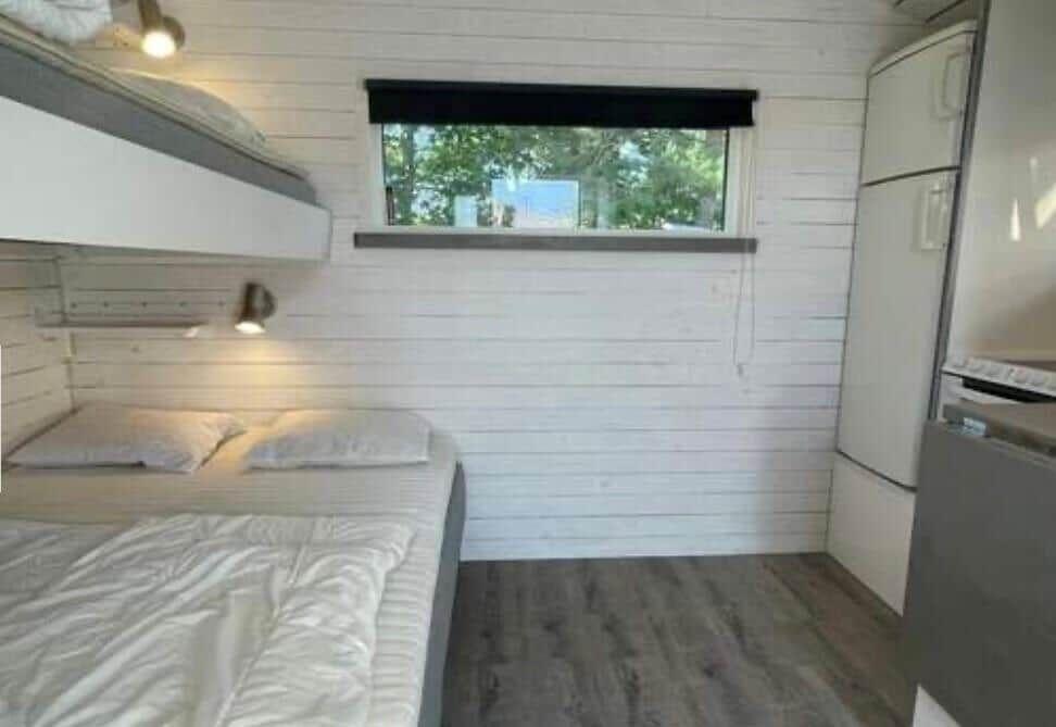 Zimmer mit Doppelbett, oberem Bett und Fenster mit Blick auf Bäume.