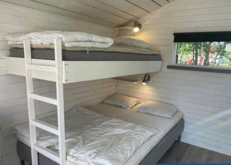 Zwei Etagenbetten mit Matratzen und Bettwäsche. Holzwand und Fenster sichtbar.