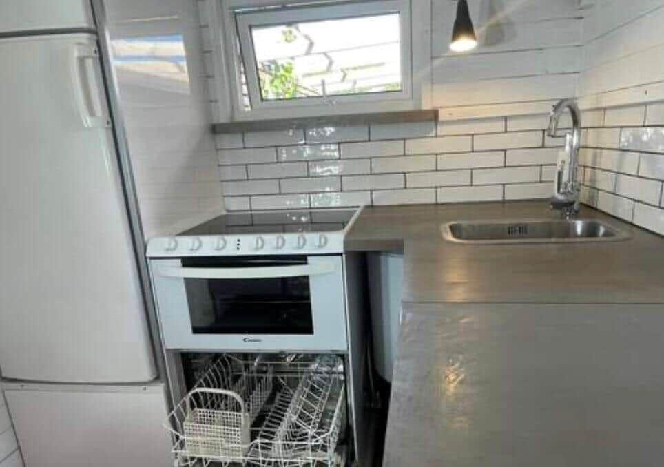 Küche mit Spüle, Herd und Kühlschrank. Weiße Fliesen und Fenster.