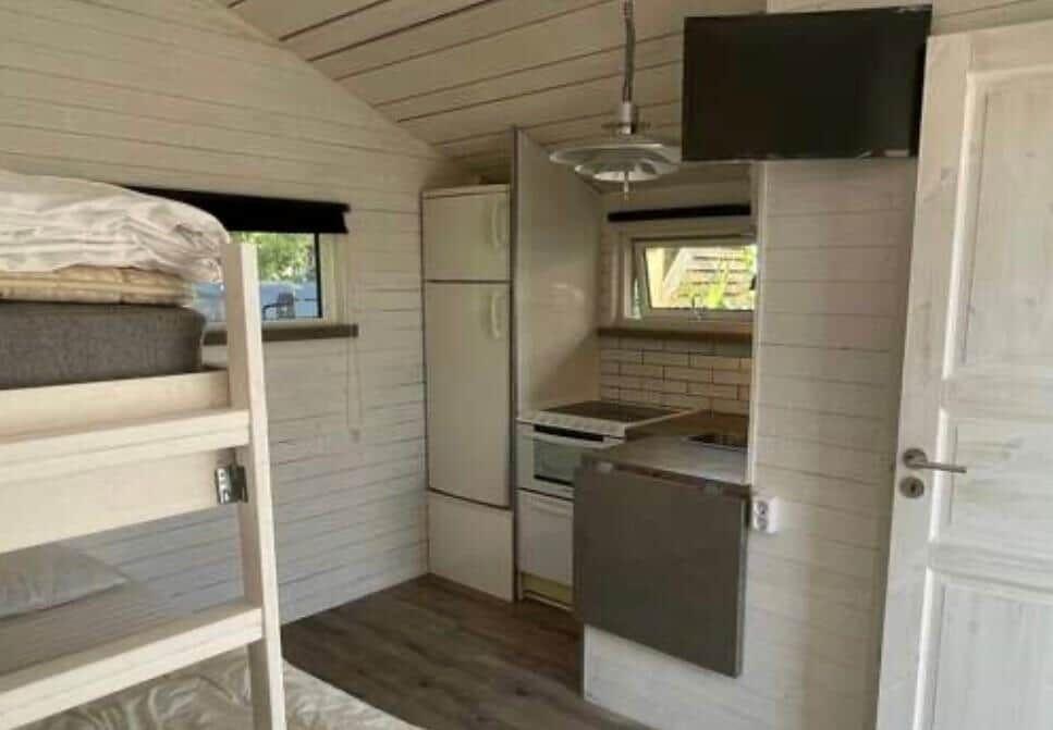 Kleines Schlafzimmer mit Doppelstockbett und Küchenbereich mit Kühlschrank und Herd.