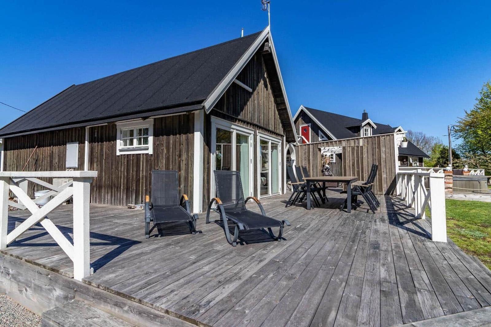 Holzterrasse mit Liegestühlen und Tisch. Hintergrund: Holzhaus mit Fenstern und Dach.