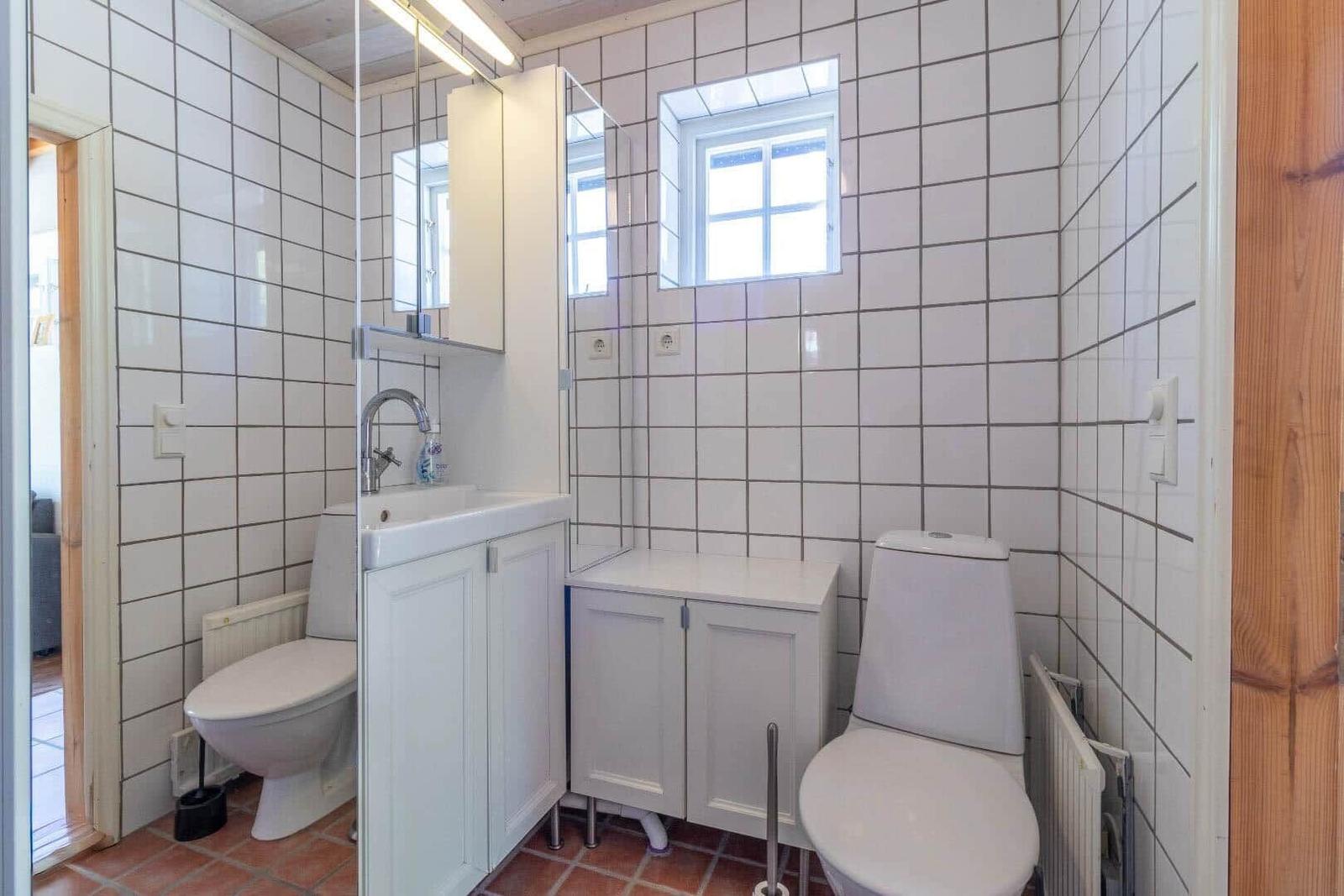Badezimmer mit Toilette, Waschbecken und Spiegelschrank. Weiße Fliesen und kleines Fenster.