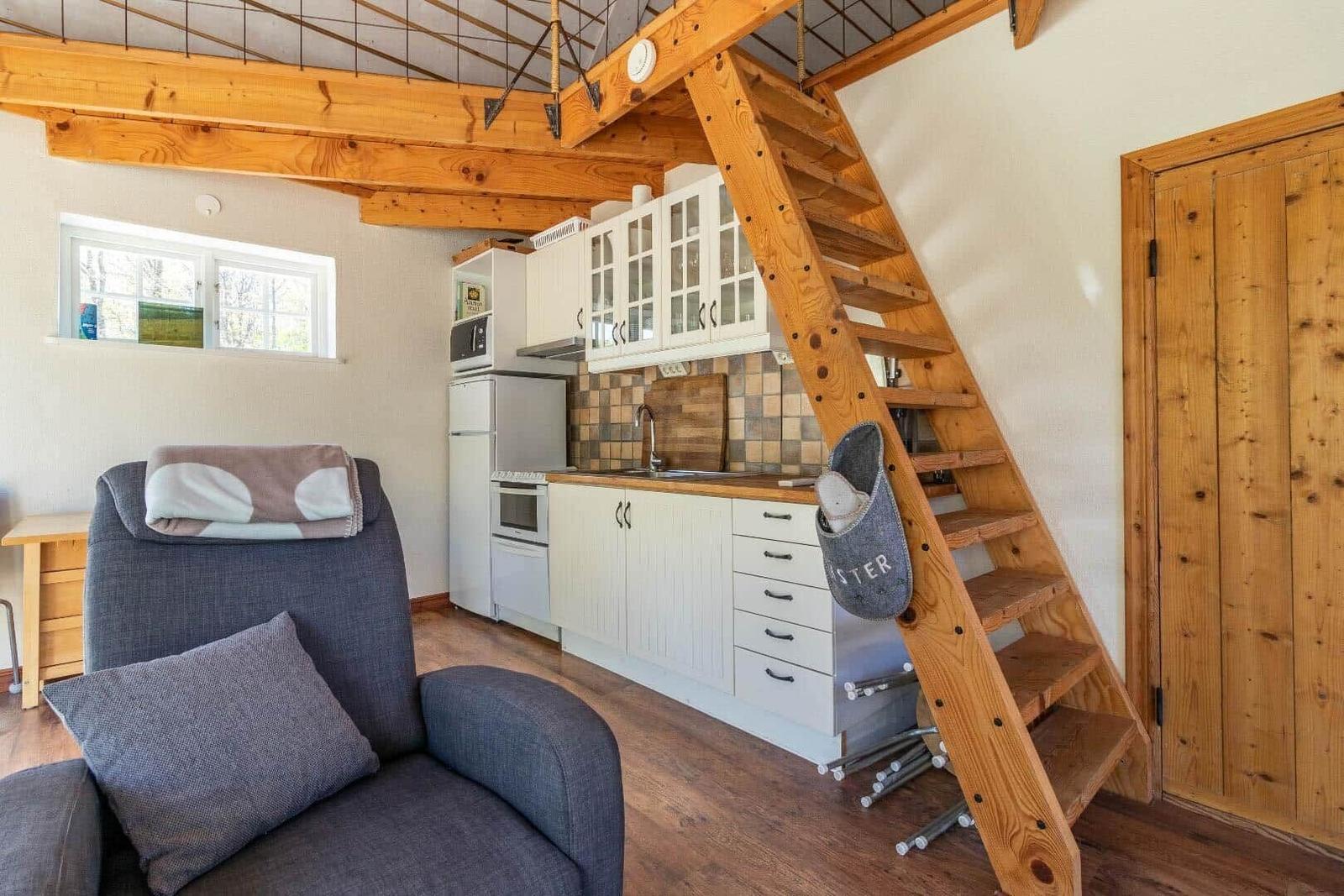 Küche mit Arbeitsplatte, Schränken und Fenster. Holztreppe führt nach oben. Sitzgelegenheit mit Kissen.