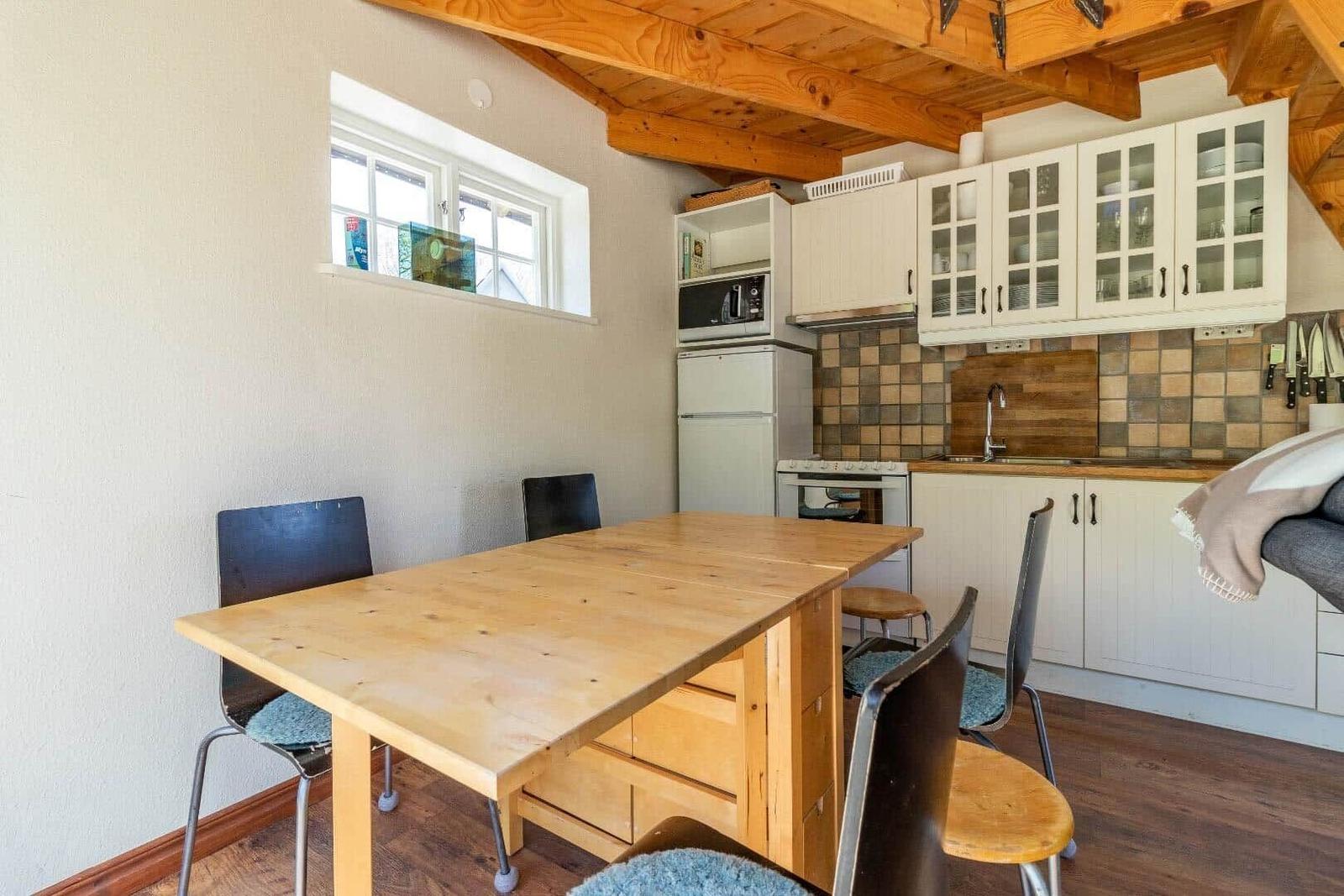 Küche mit Essbereich, Holztisch, weißen Schränken und Holzbalkendecke.