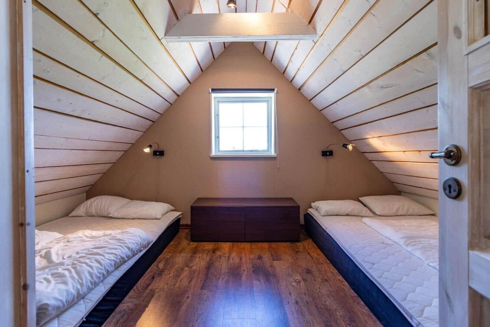 Zwei Betten unter Dachschrägen mit Holzfußboden und kleinem Fenster.
