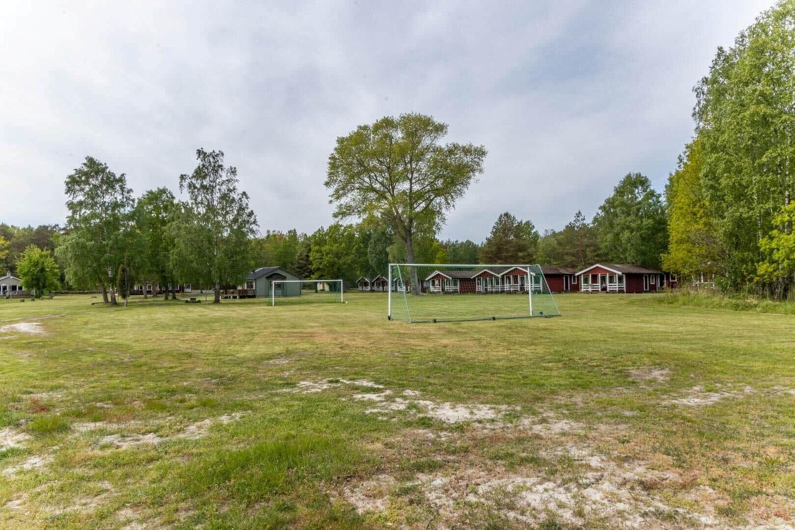 Grünes Feld mit Fußballtor und Holzhütten im Hintergrund.