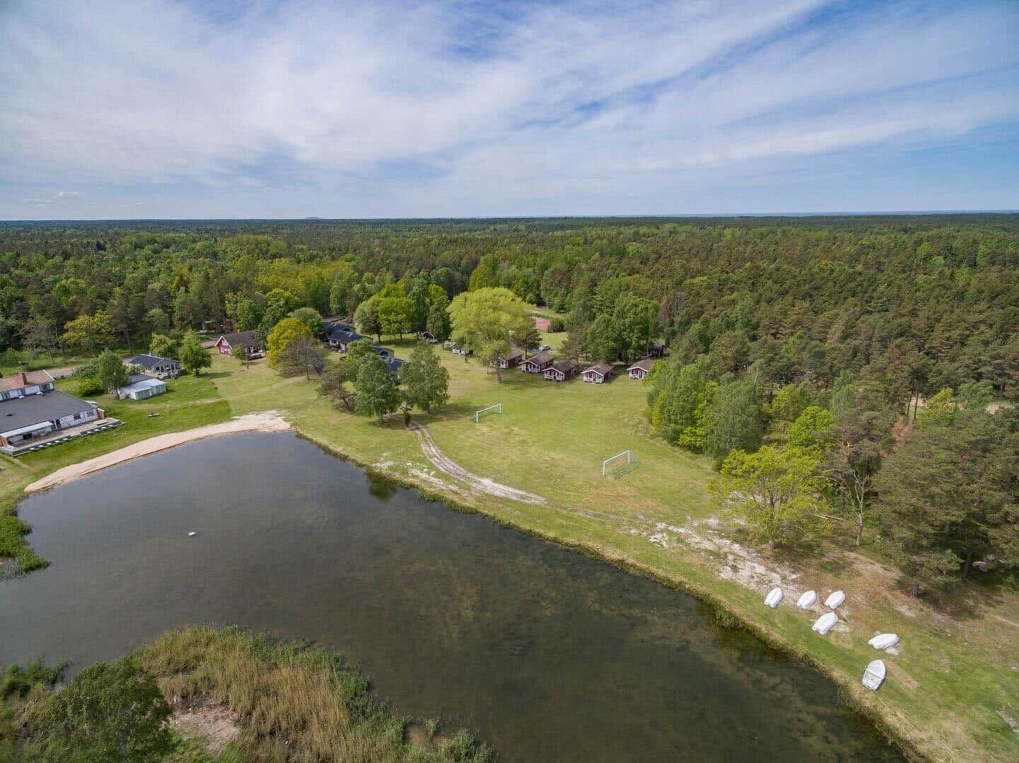 Liegenschaft mit See, Booten und Wald. Mehrere Häuser und ein Fußballtor sind sichtbar.