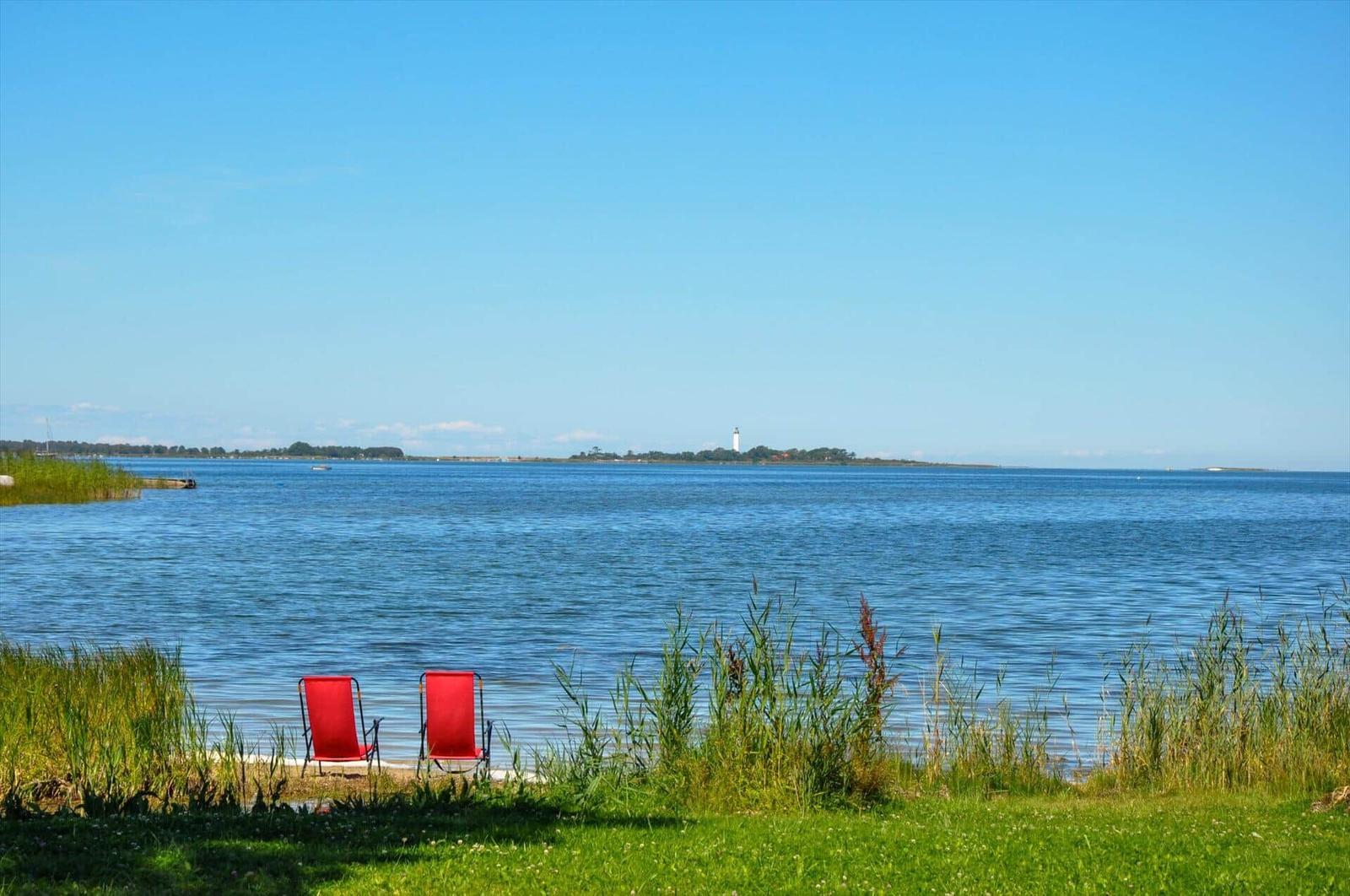 Zwei rote Liegestühle am Ufer mit Blick auf einen Leuchtturm.