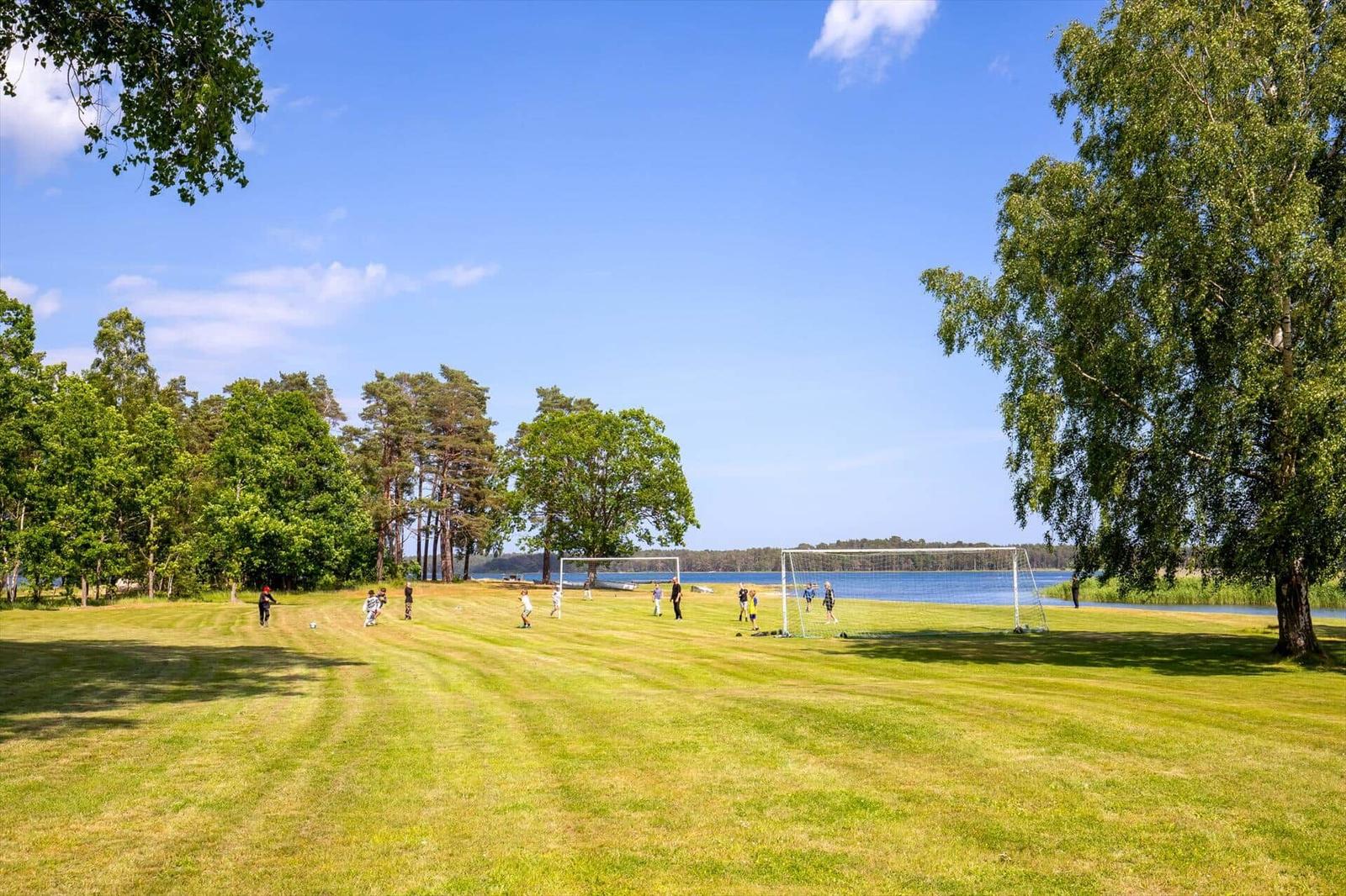 Grünes Feld mit Fußballtoren am See. Menschen spielen im Freien.