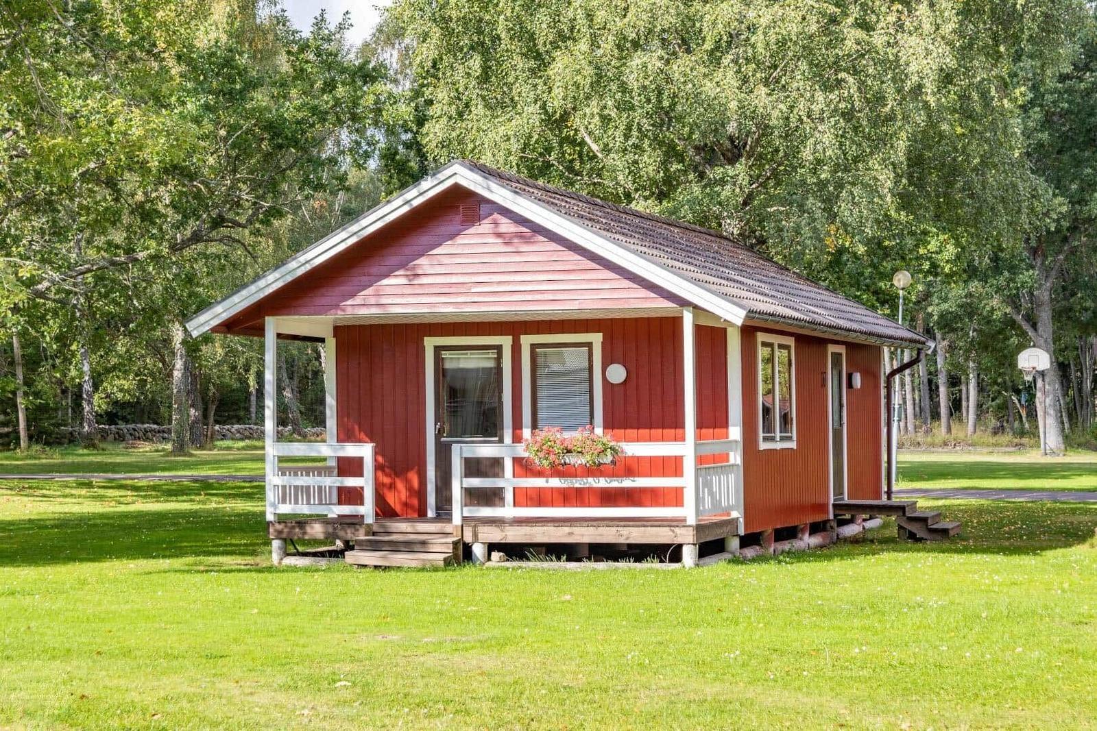Rotes Holzhaus mit weißem Vordach und Blumenkasten auf grünem Rasen.