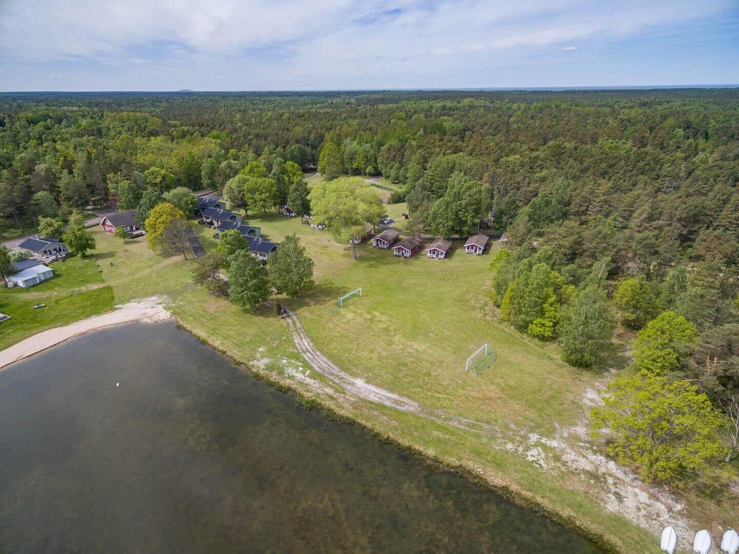 Liegenschaft mit Hütten am See und Wald. Fußballtore und Sandstrand sichtbar.