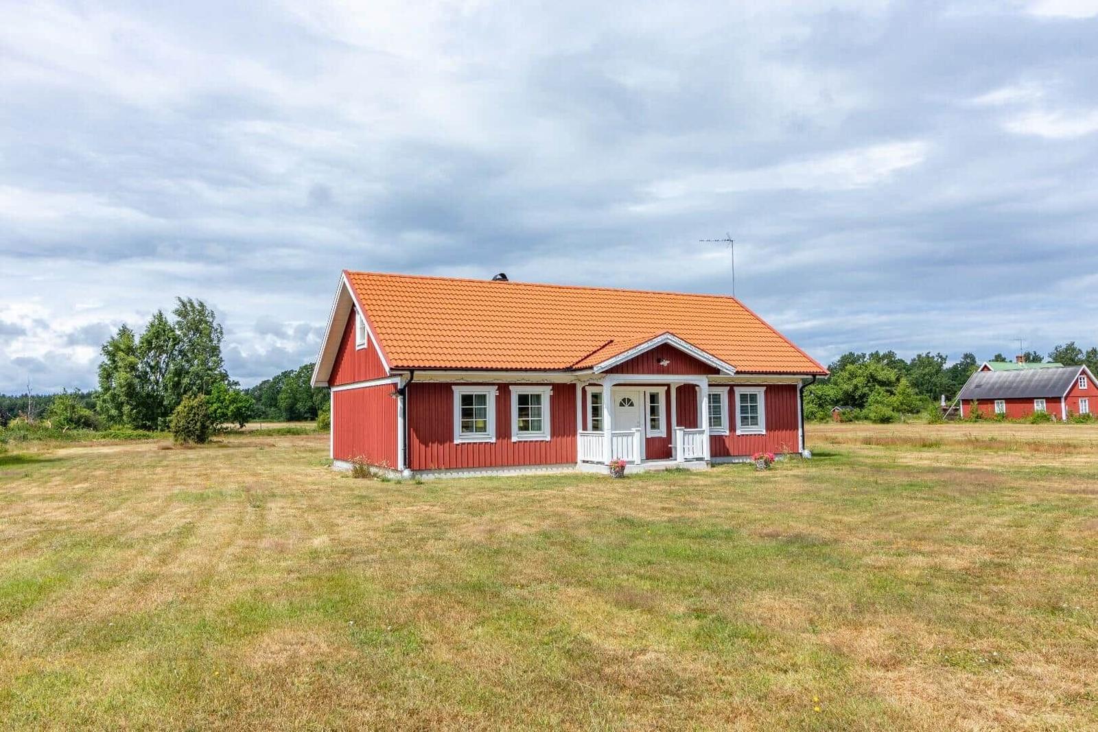 Rotes Holzhaus mit orangefarbenem Dach auf grünem Feld