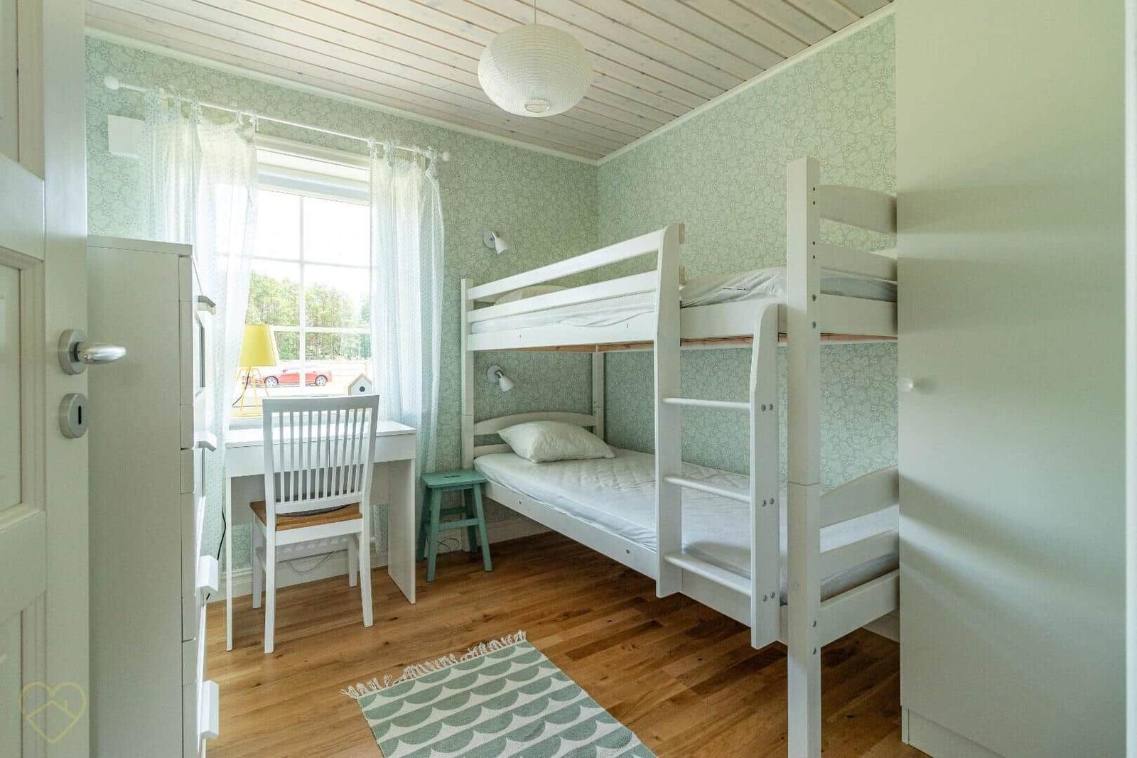 Zimmer mit Doppelstockbett, Schreibtisch und Fenster.