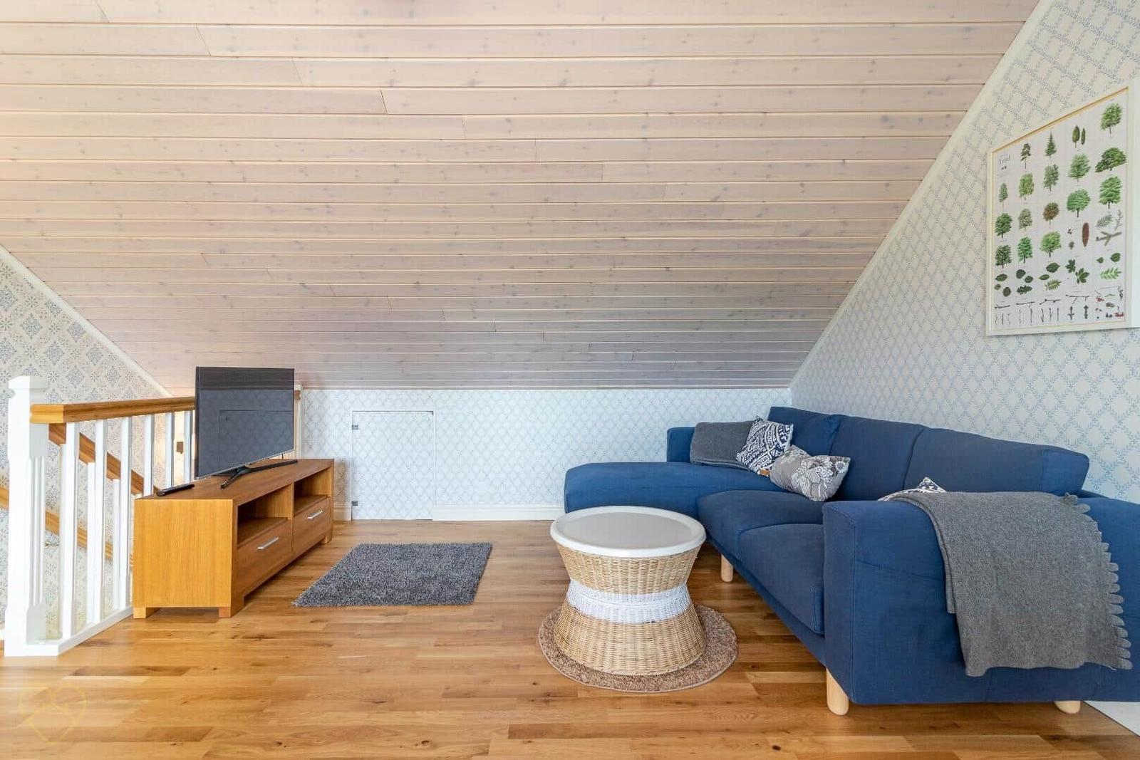 Ein Wohnzimmer mit blauem Sofa, Holzboden und schrägen Holzwänden.