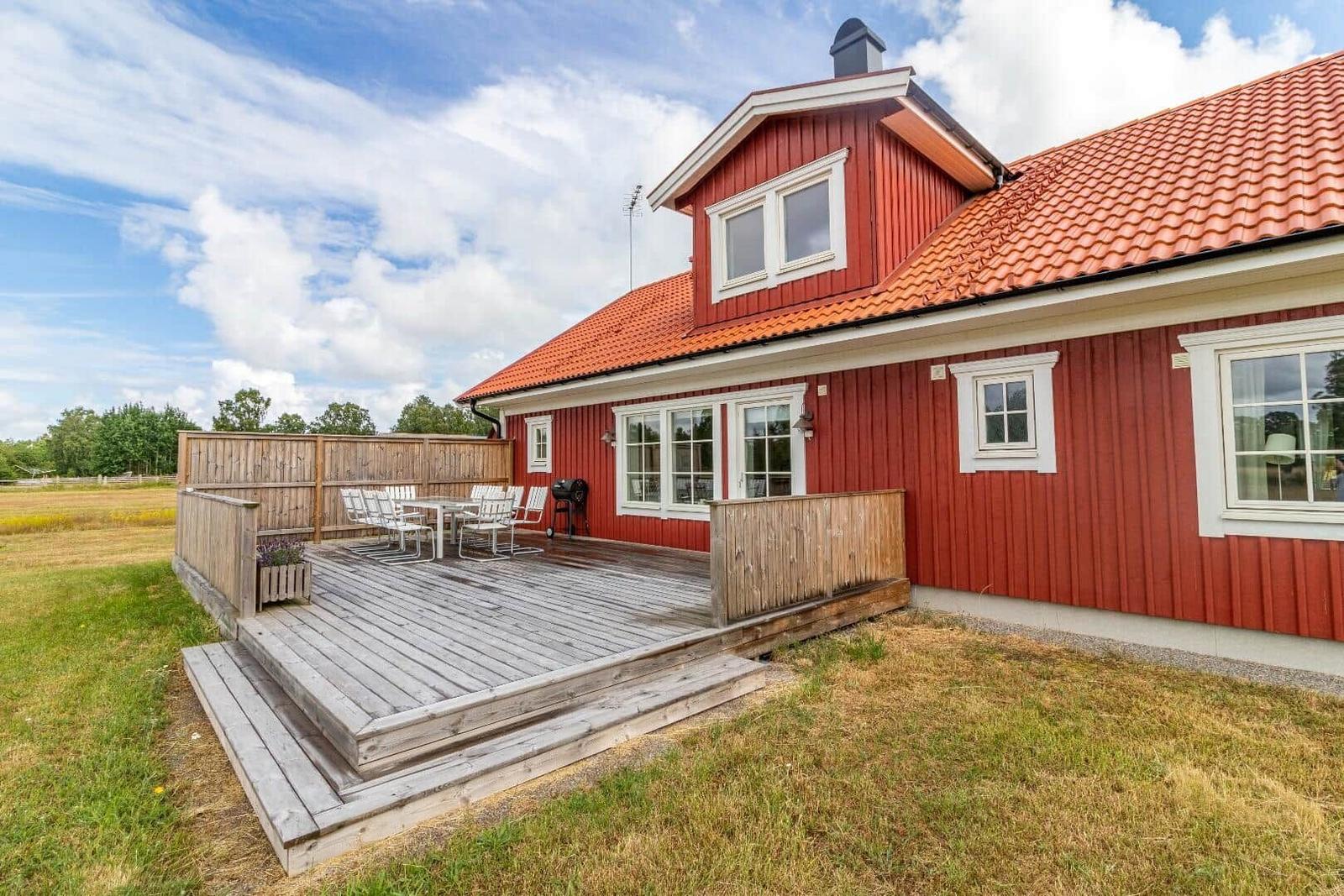 Rotes Holzhaus mit Terrasse, Grill und Garten.