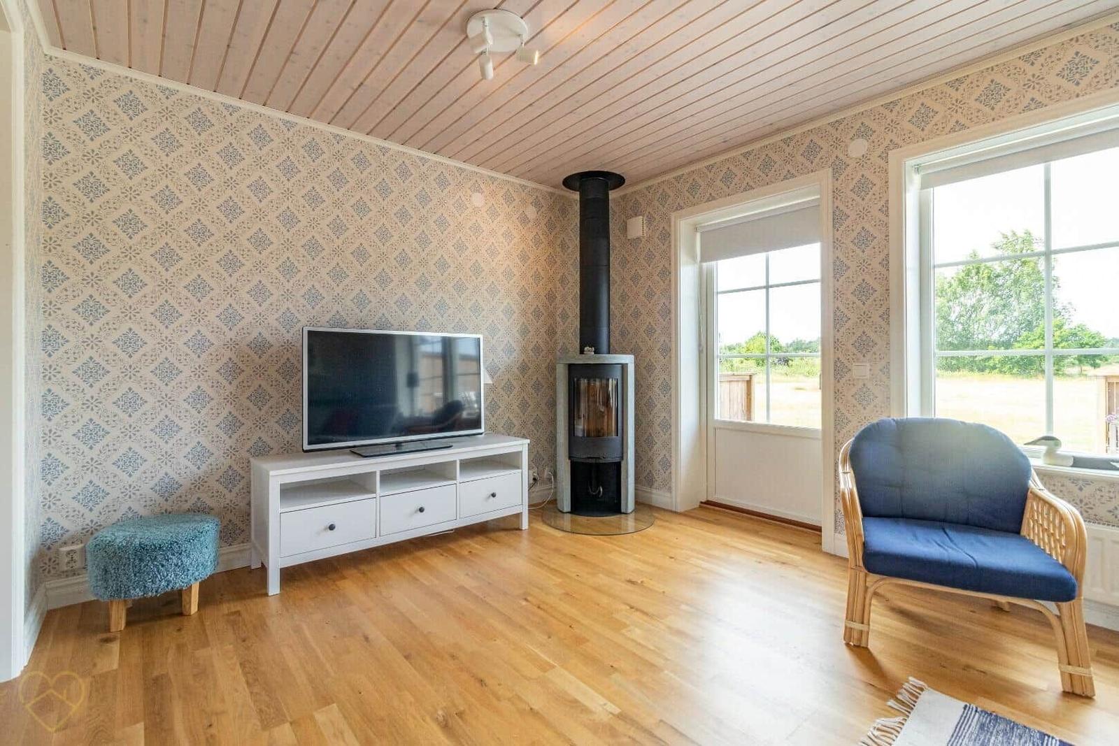 Wohnzimmer mit Holzboden, Fernseher, Kamin und blauem Sessel.