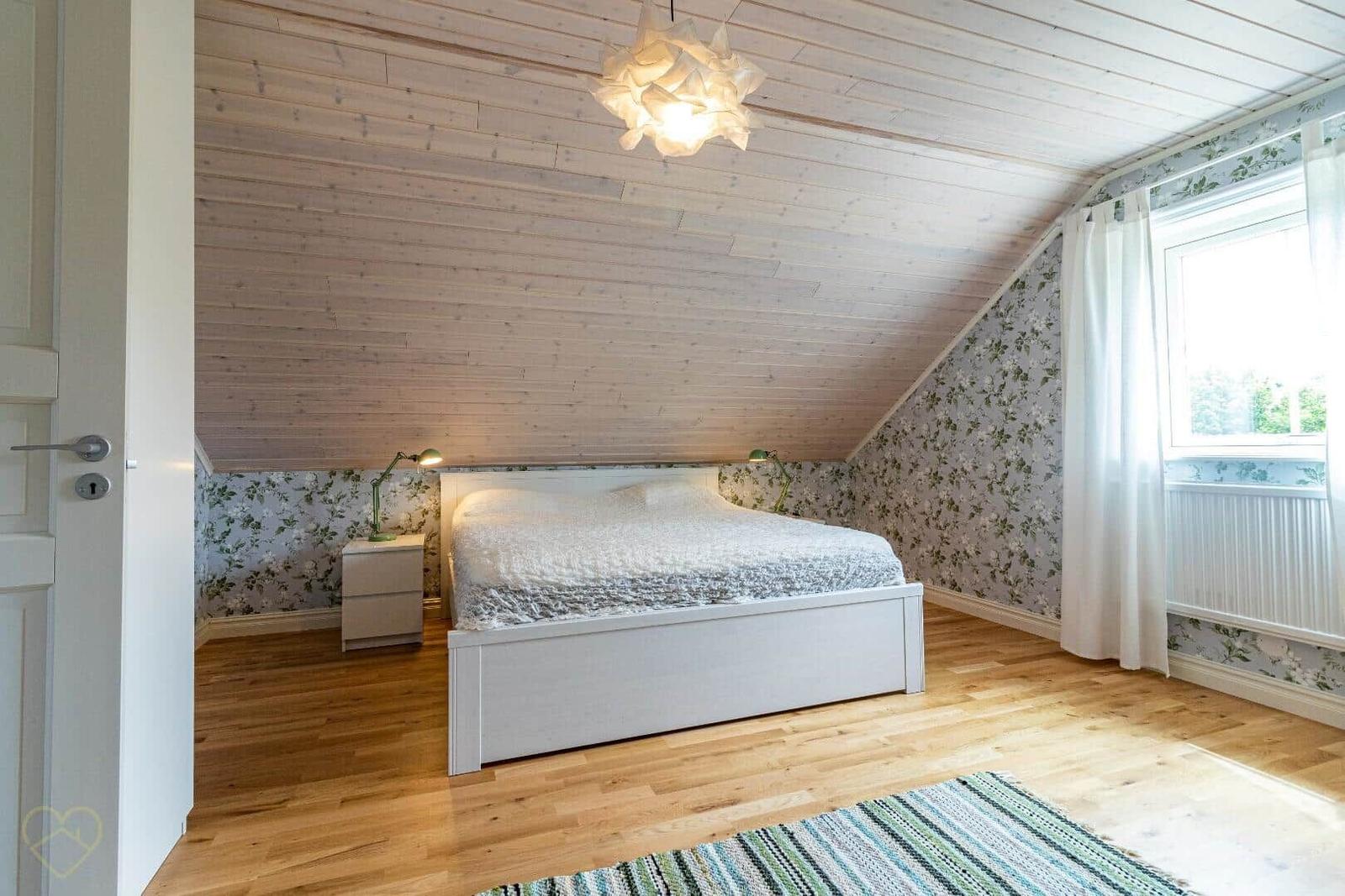 Schlafzimmer mit Holzdecke, floraler Tapete und weißem Bett.