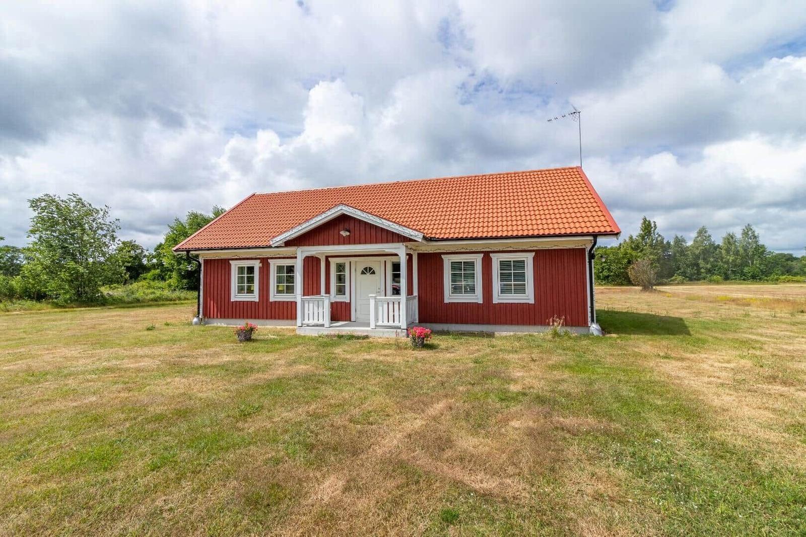 Rotes Holzhaus mit weißem Vordach und rotem Dach, umgeben von Gras und Bäumen.