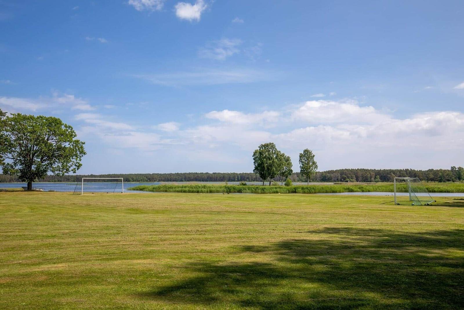 Grünes Feld mit zwei Toren am Ufer eines Sees unter blauem Himmel.