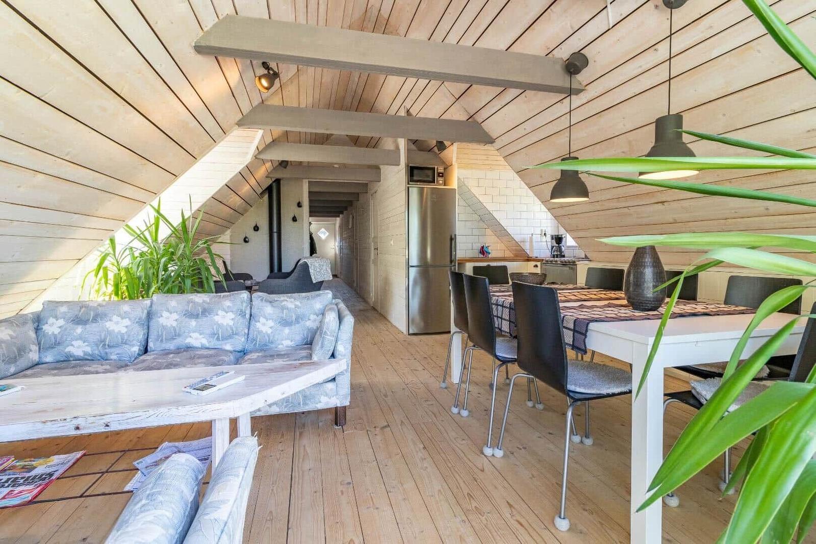 Wohn- und Essbereich mit Holzdecke, Sofa, Tisch und Küchenspüle.